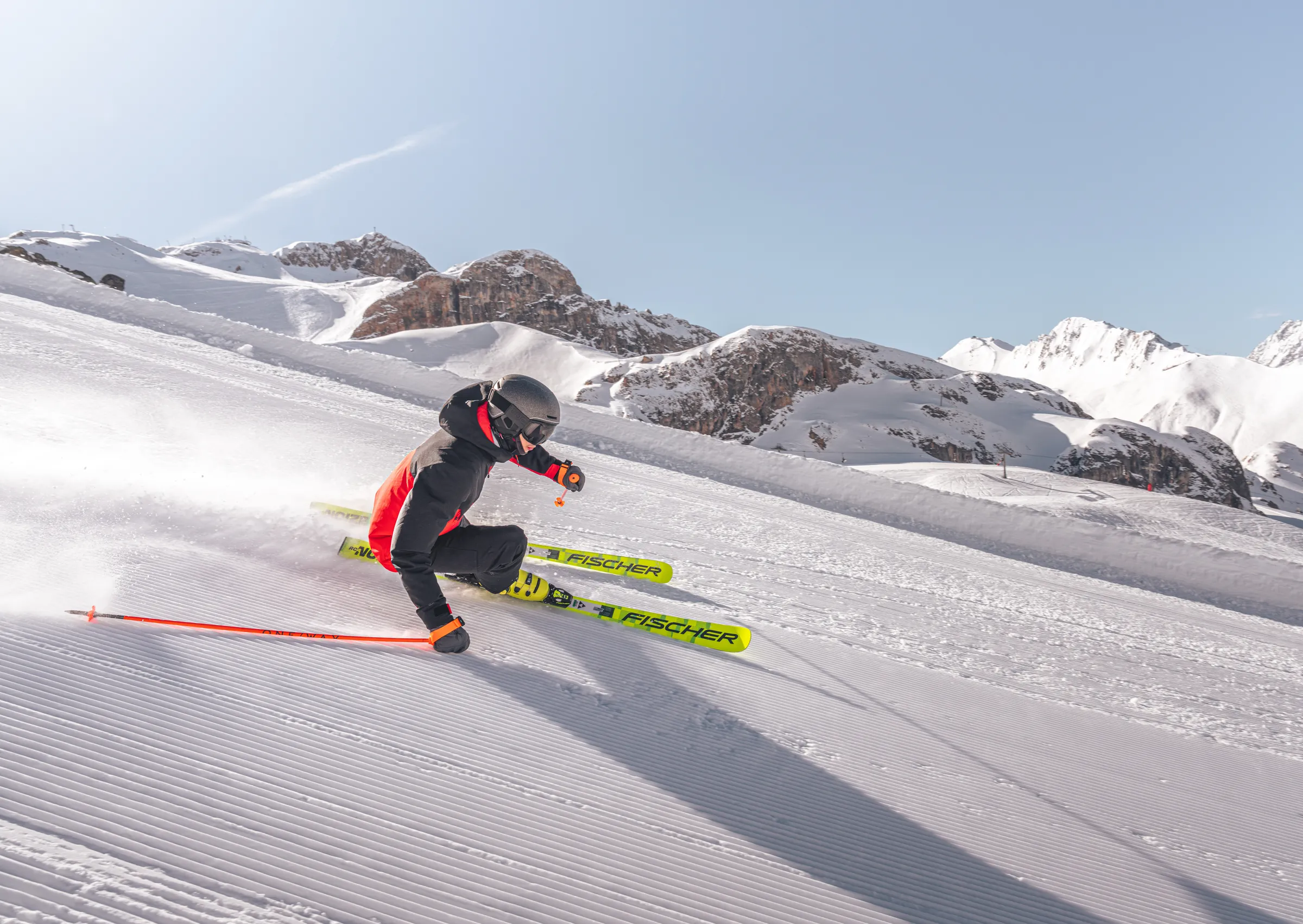 Skifahrer im Carving-Schwung auf einer frisch präparierten Piste im Skigebiet Ischgl-Samnaun, dahinter verschneite Gipfel der Silvretta