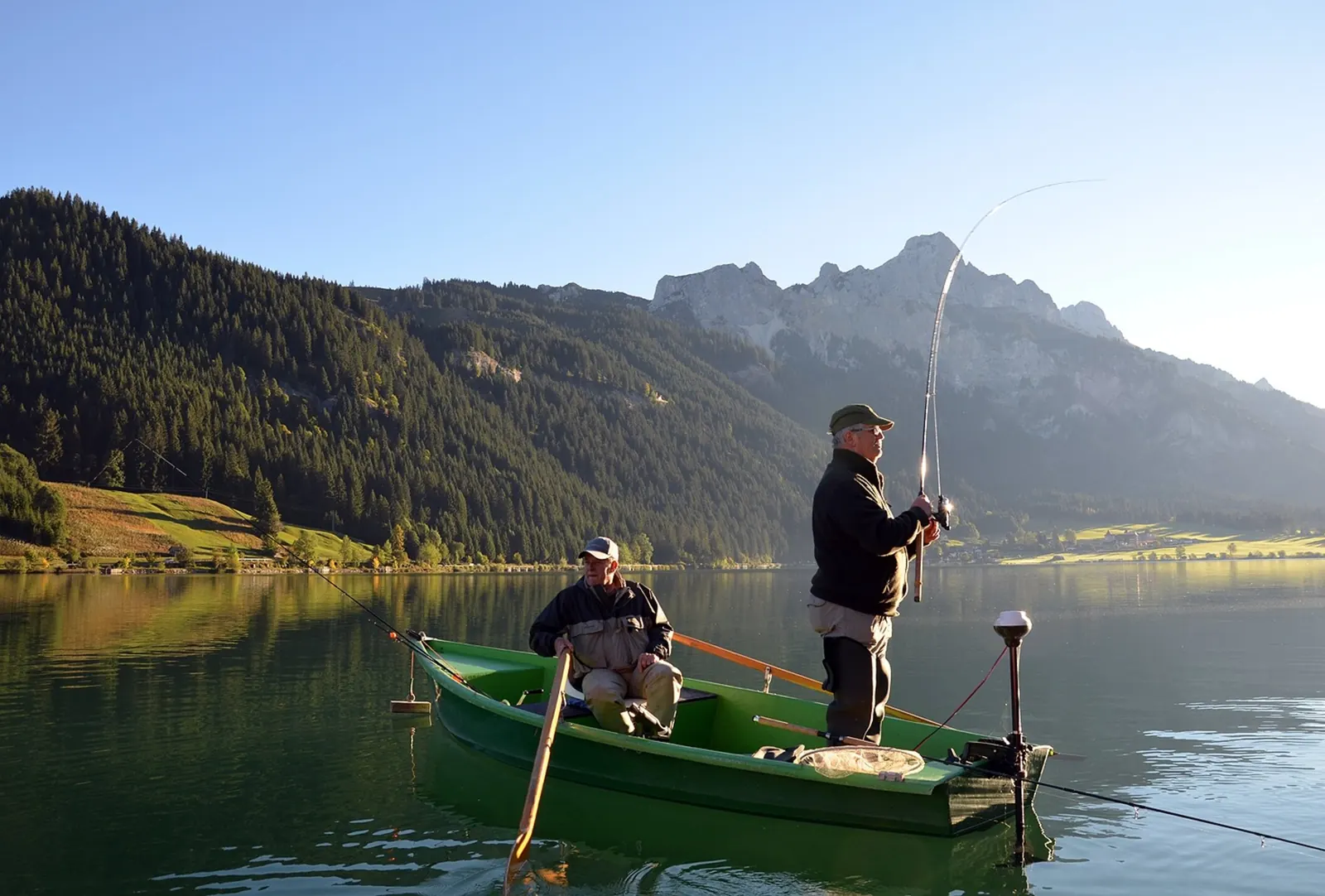 Zwei Angler im Boot auf dem Haldensee, dahinter bewaldete Hänge und die Felsen der Tannheimer Berge