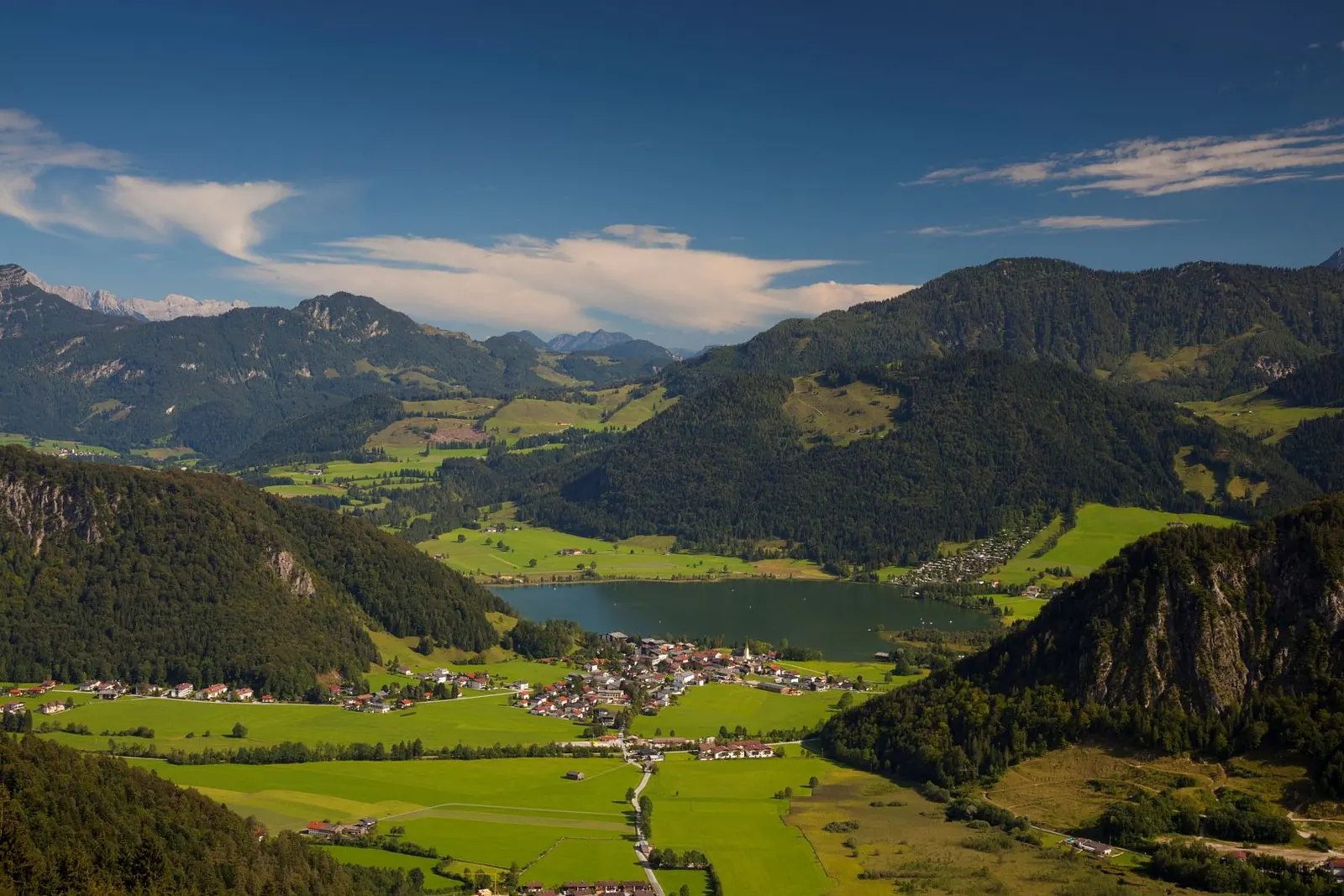 Blick von oben auf den Walchsee und das Dorf Walchsee zwischen grünen Wiesen und bewaldeten Bergen