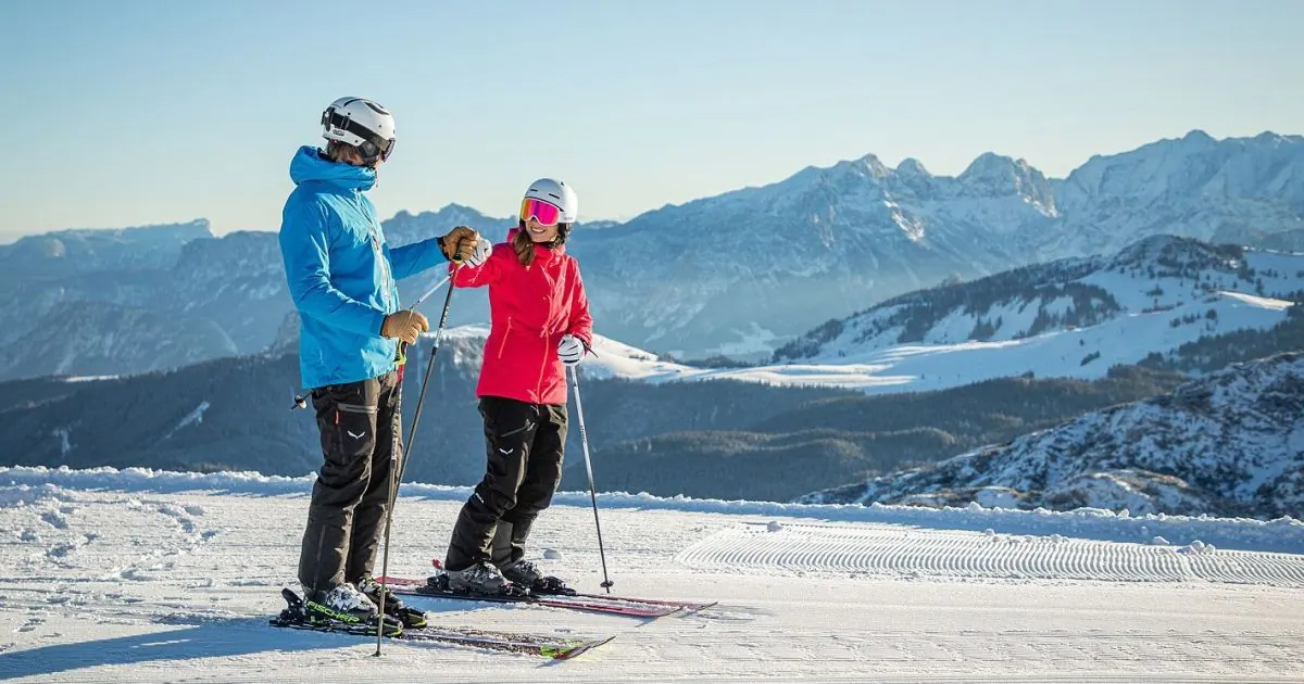 Zwei Skifahrer auf einer frisch präparierten Piste der Steinplatte, dahinter verschneite Berge im Morgenlicht