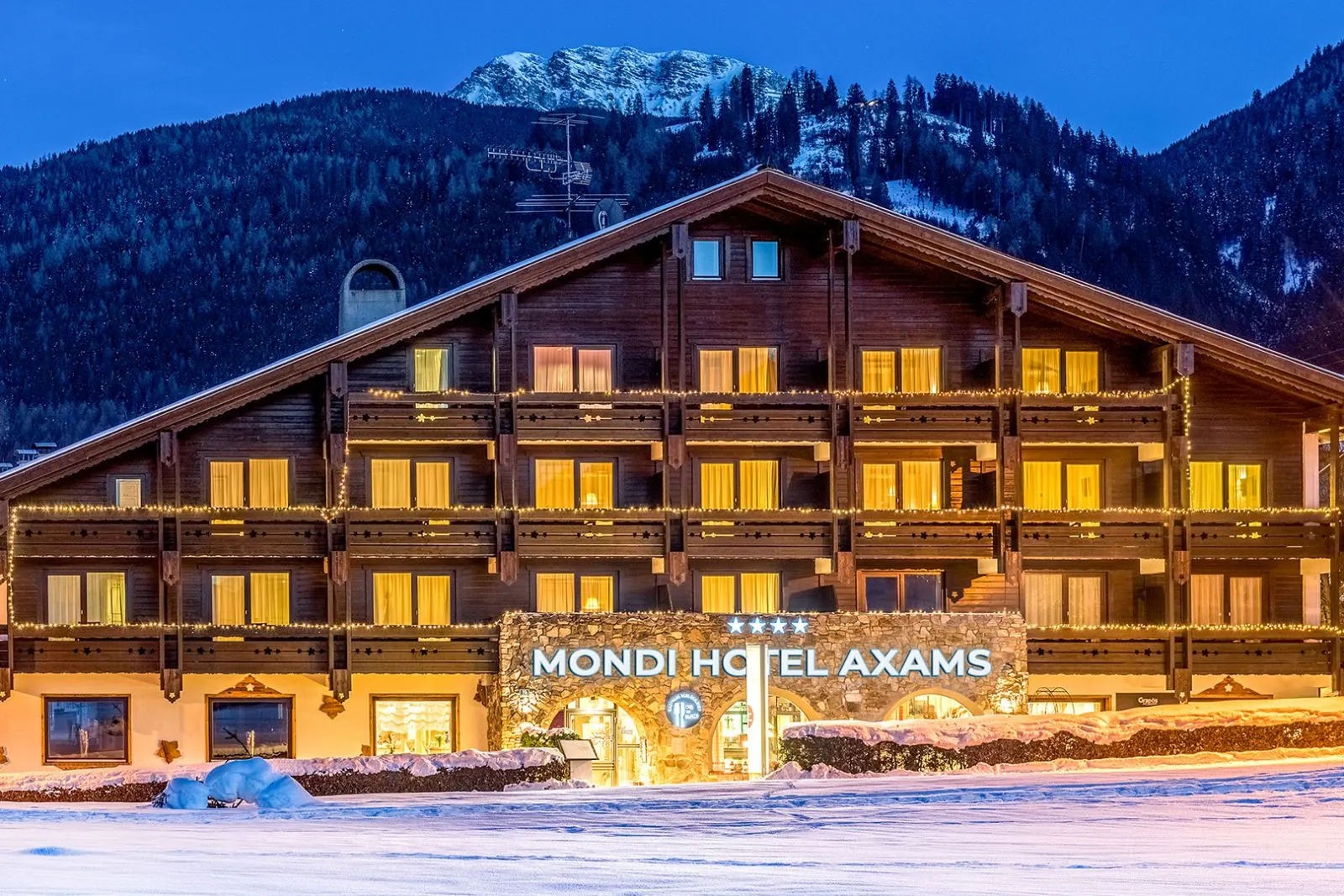 Winteransicht des MONDI Hotel Axams am Abend mit beleuchteten Balkonen und verschneiten Bergen dahinter