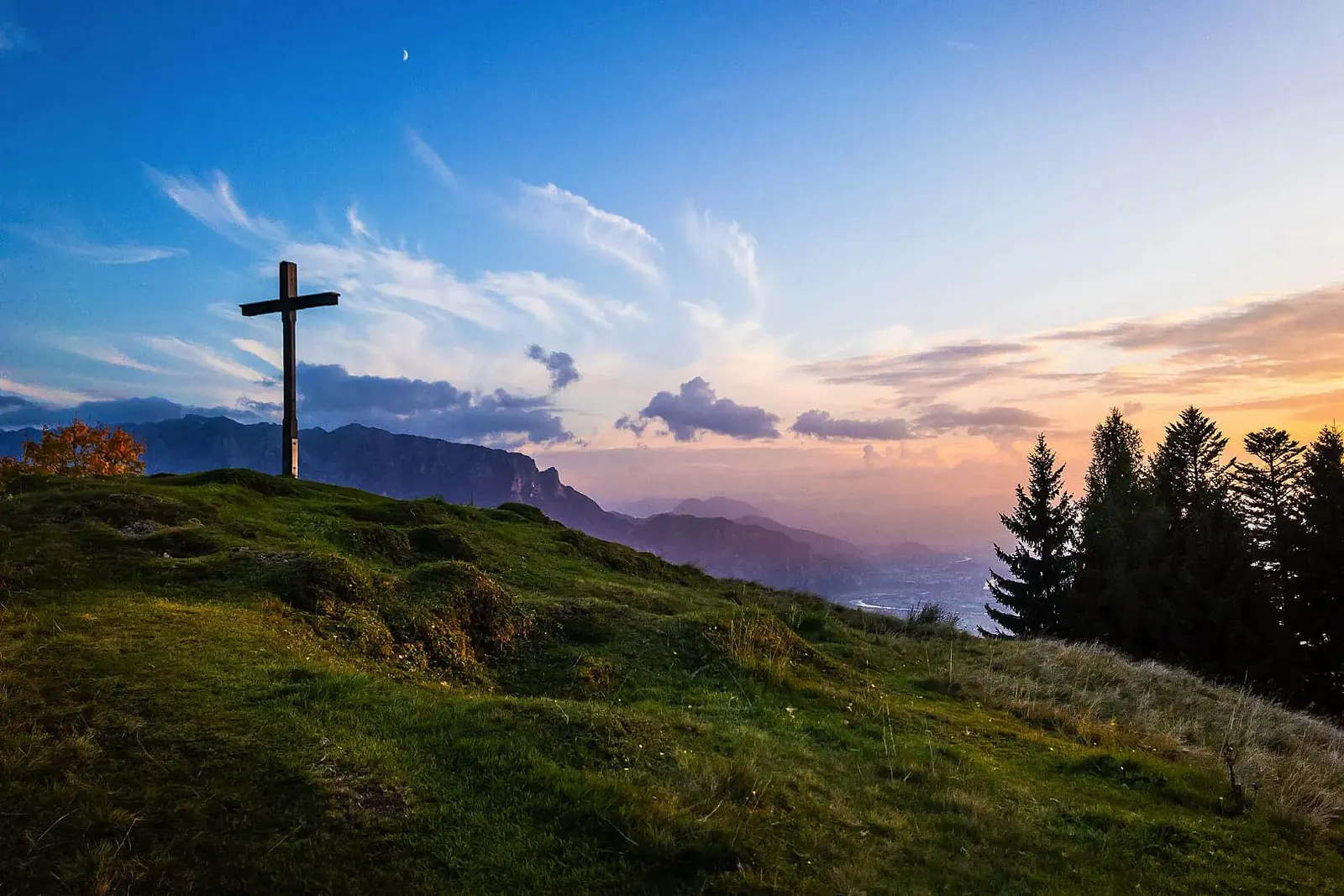 Gipfelkreuz auf der Karspitze bei Rettenschöss über grünen Almhängen im Abendlicht