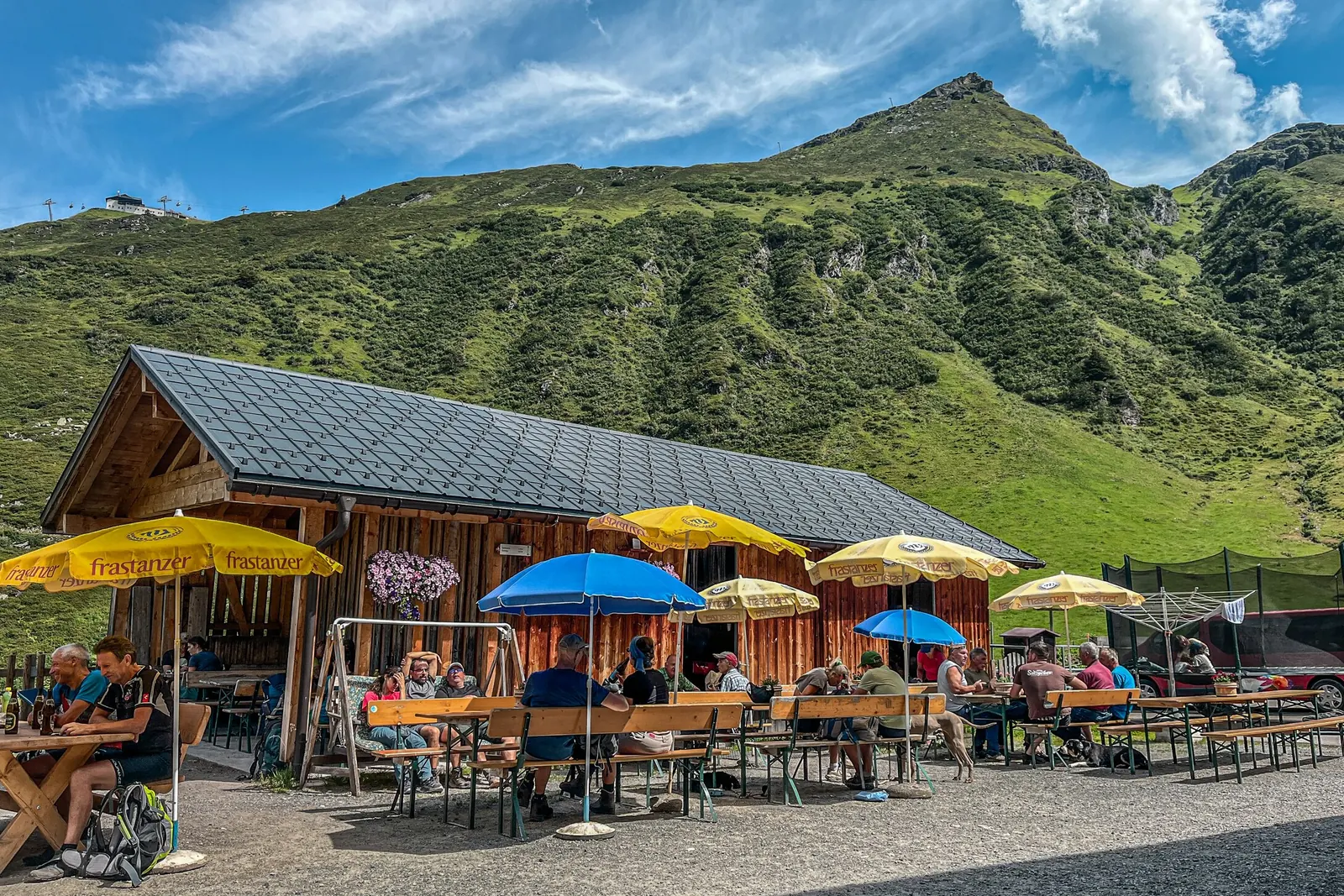 Bewirtschaftete Alpe Nova mit Sonnenschirmen und grünen Berghängen