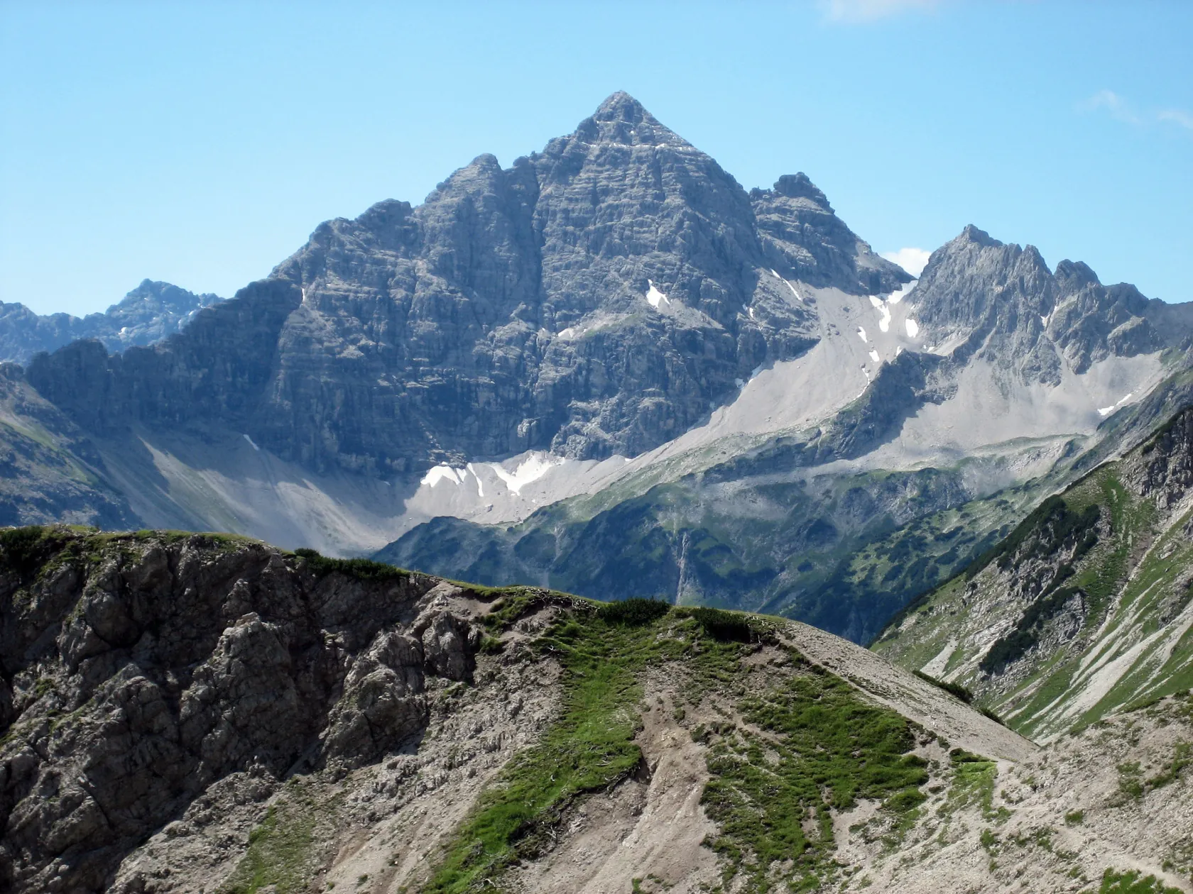 Felsiger Hochvogel mit grünen Hängen im Vordergrund und einzelnen Schneeresten