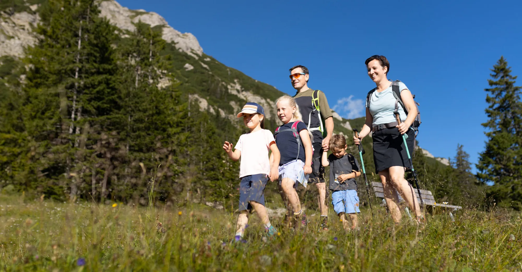 Familie auf einem Wiesenweg vor Wald und felsigen Hängen im Oberjocher Wandergebiet