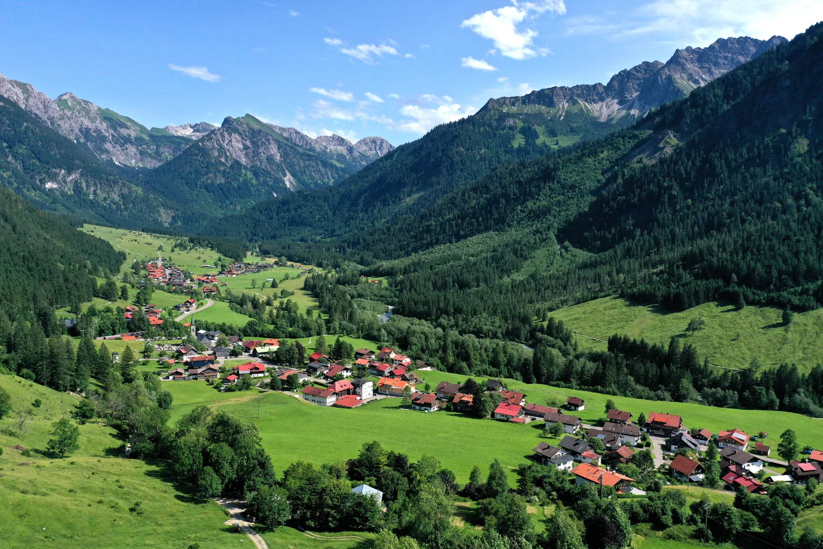 Hinterstein mit grünen Wiesen und bewaldeten Hängen vor den Allgäuer Bergen