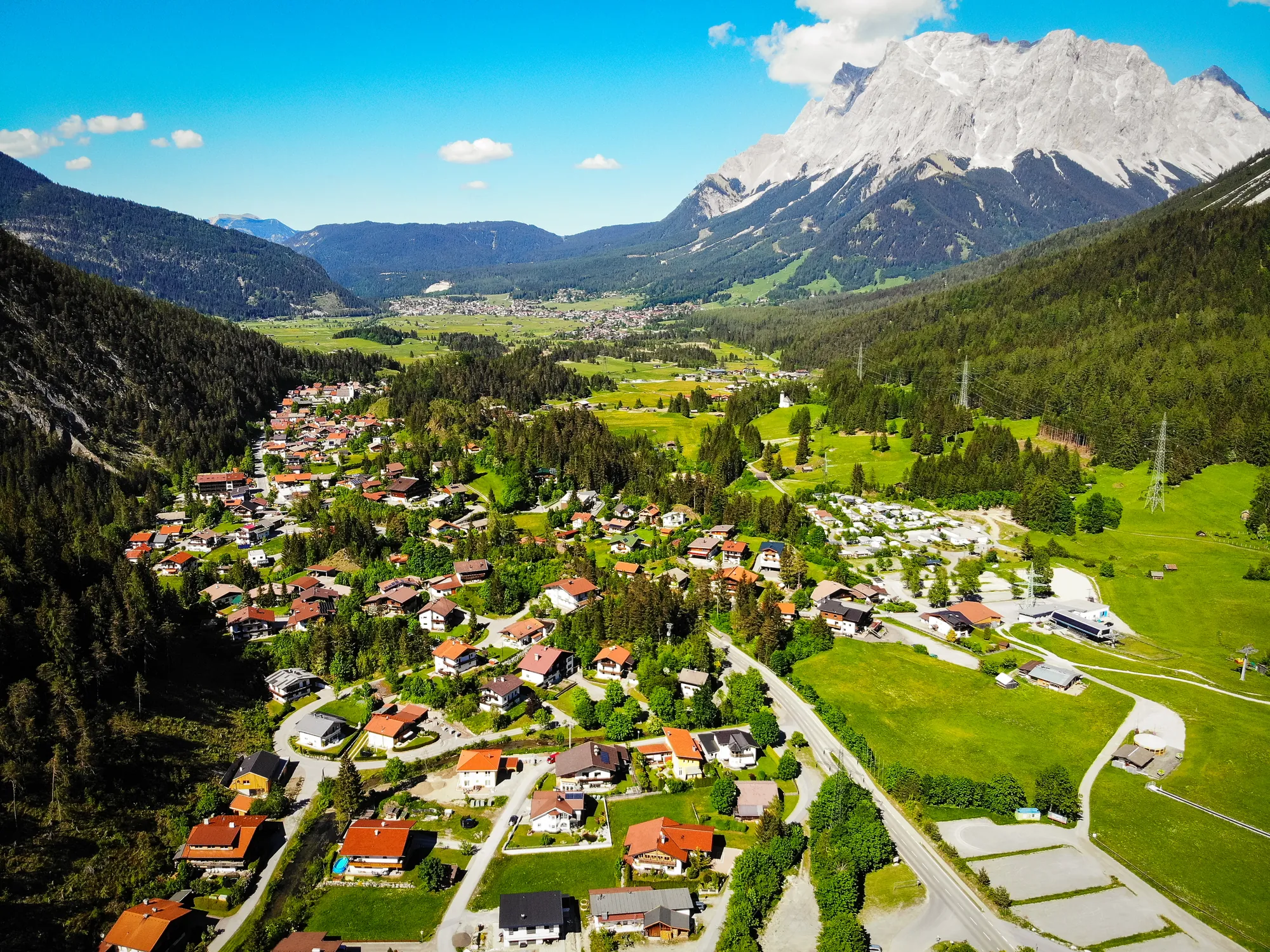 Biberwier mit grünen Wiesen und Häusern zwischen bewaldeten Hängen vor dem Wettersteinmassiv.