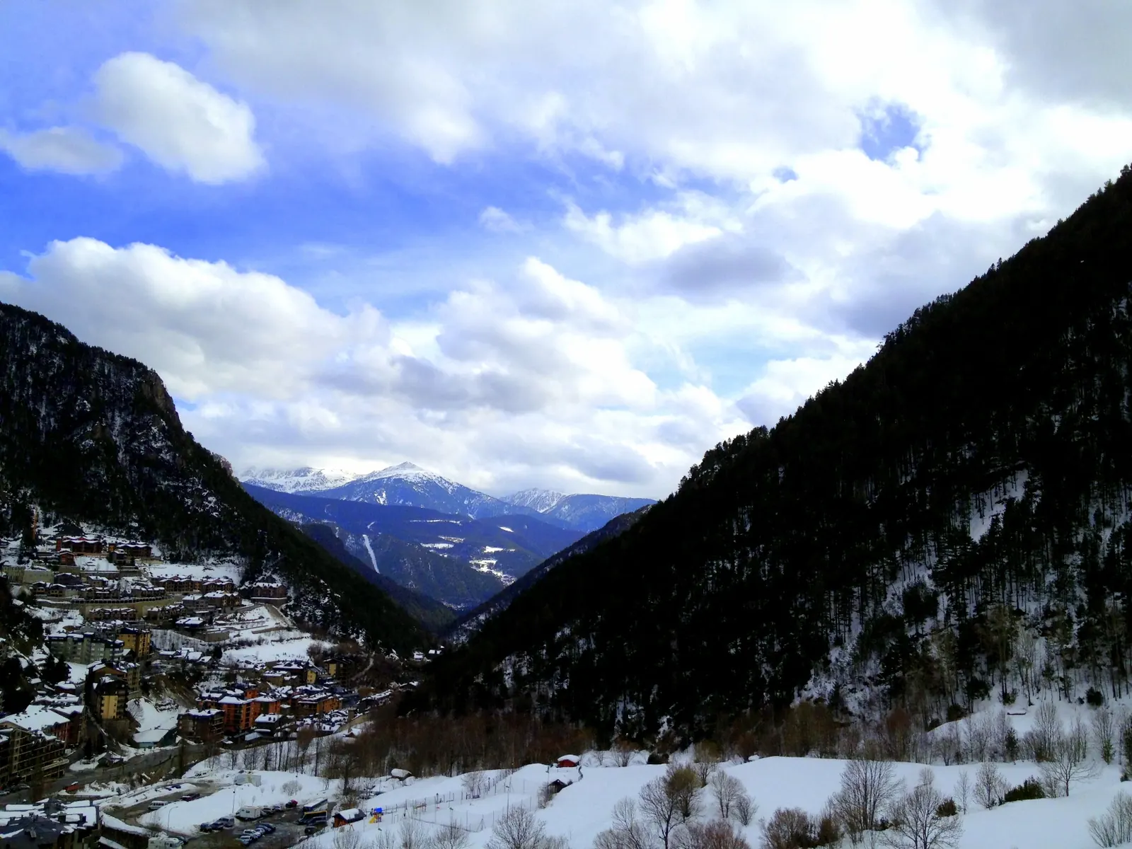 Verschneites Tal von Arinsal mit Häusern am linken Hang, bewaldeten Bergflanken und schneebedeckten Gipfeln im Hintergrund