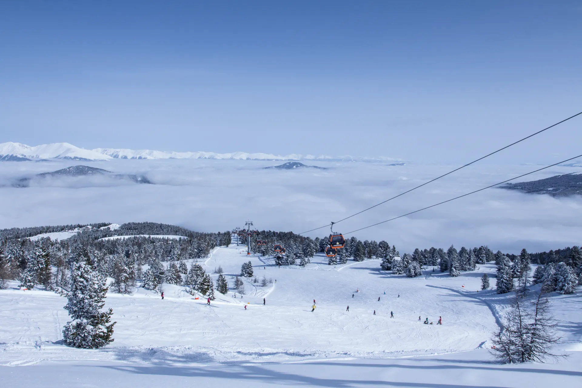 Blick von der Bergstation am Kreischberg über Piste und Gondelbahn auf ein Nebelmeer und verschneite Gipfel
