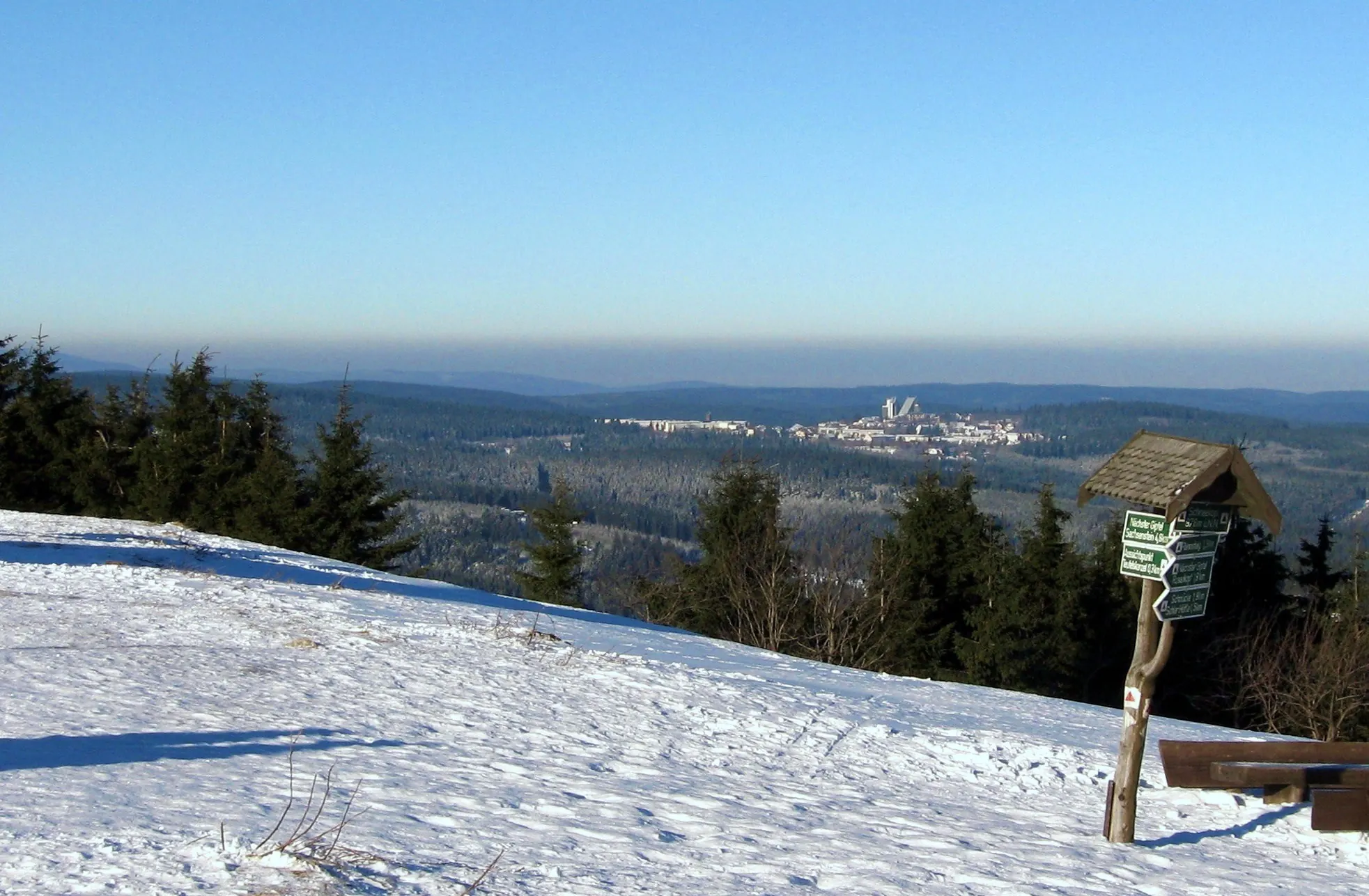 Verschneiter Gipfel des Schneekopfs im Thüringer Wald mit Wegweiser und Blick über Wälder auf Oberhof