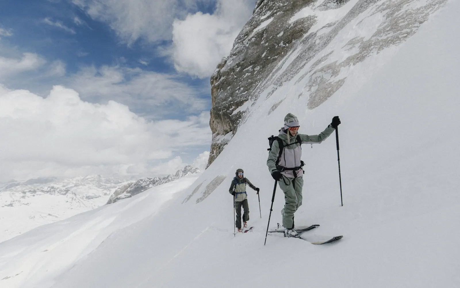 Skitourengeherin im mintgrünen Karpos Squall Set im Aufstieg unter einer Felswand an der Marmolada