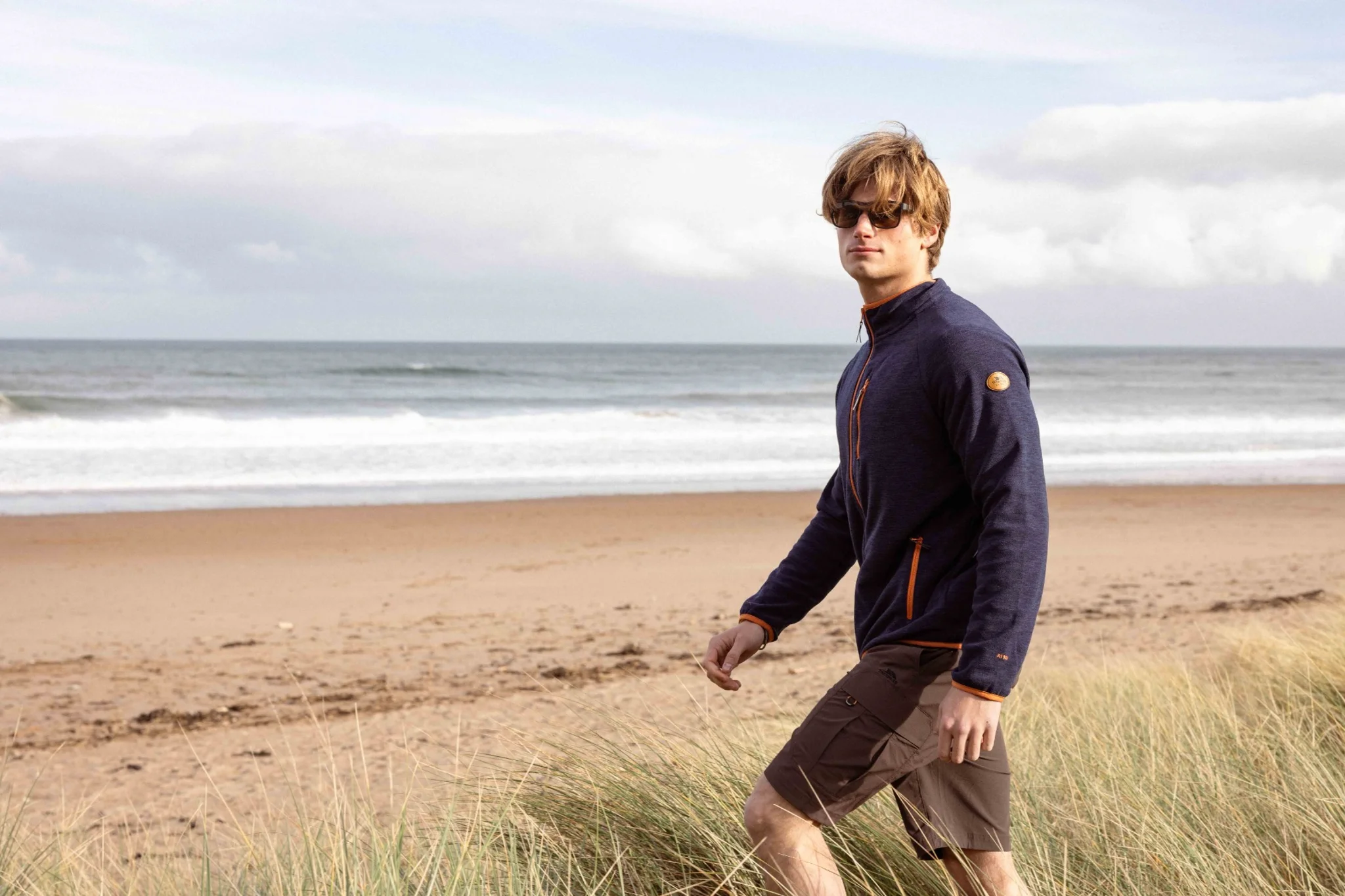 Mann in Outdoor-Bekleidung bei windigem Wetter am Strand. 