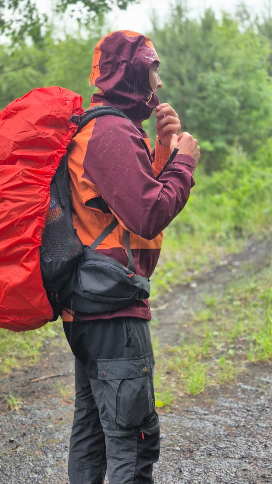 Produkttester mit geschlossener Kapuze der Ternua Klimmer Jacket im Regen auf einem Waldweg