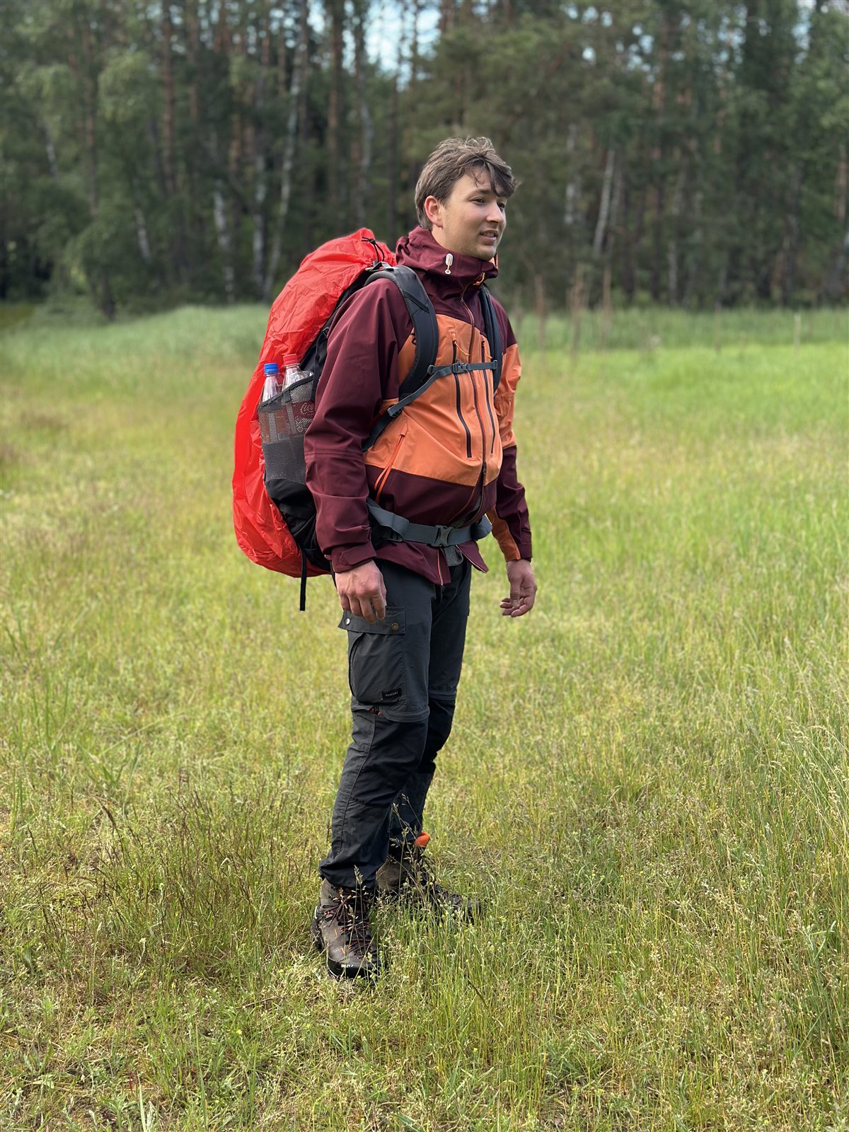 Produkttester mit Rucksack in der Ternua Klimmer Jacket auf einer Wiese am Waldrand