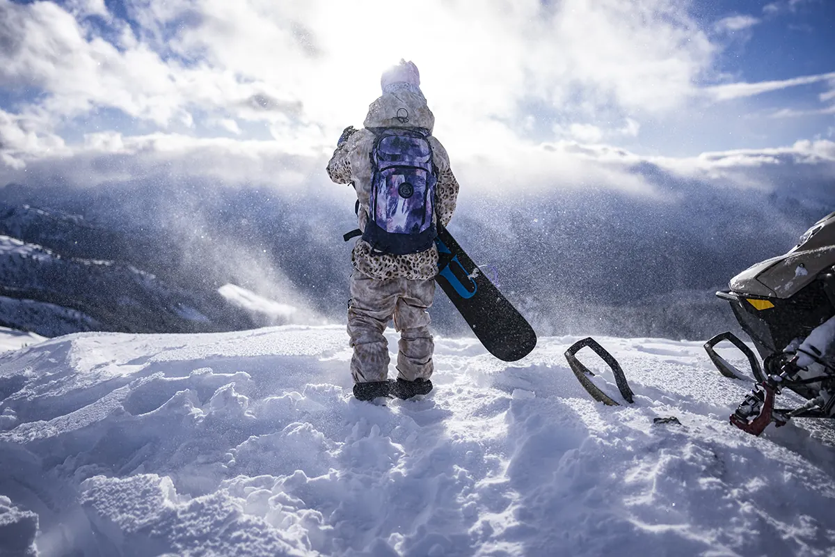 Snowboarderin mit Dakine-Rucksack und Board auf einem verschneiten Gipfel