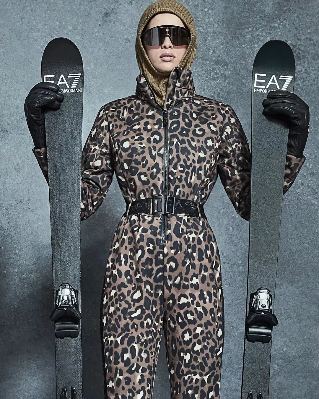 Frau im taillierten Skianzug mit Leopardenmuster und Gürtel, links und rechts je ein EA7-Ski
