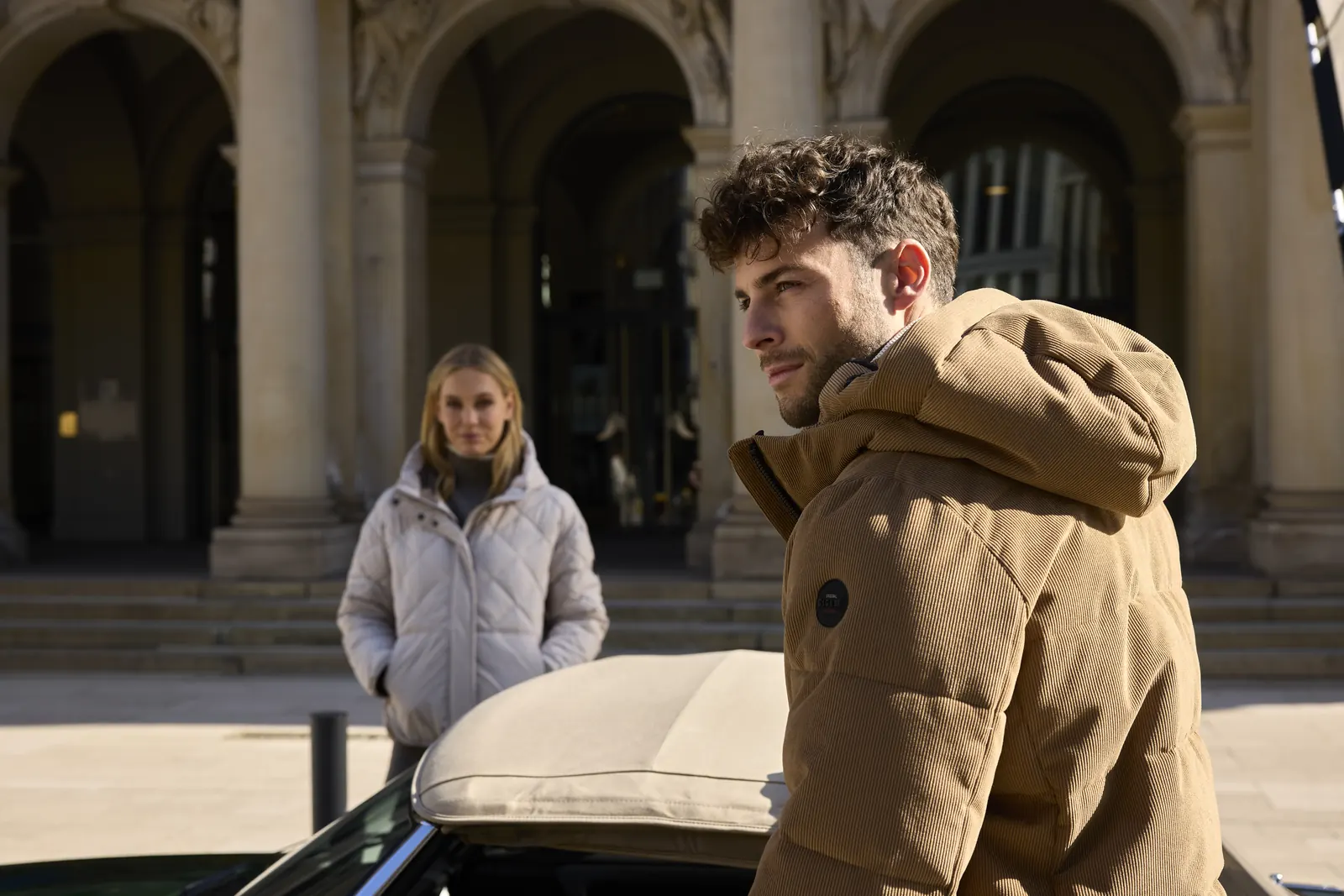 Mann in braunem Parka mit Kapuze von G.I.G.A. DX, im Hintergrund eine Frau in heller Jacke