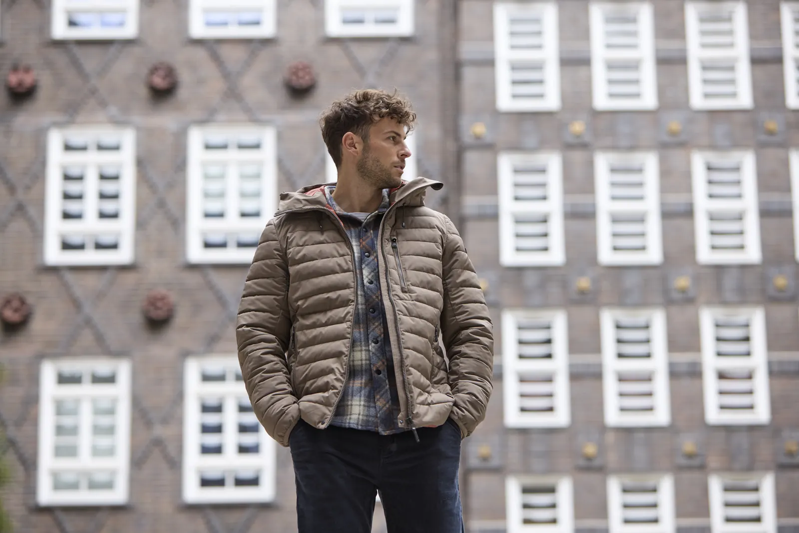 Mann in brauner Steppjacke von G.I.G.A. DX vor einer Backsteinfassade
