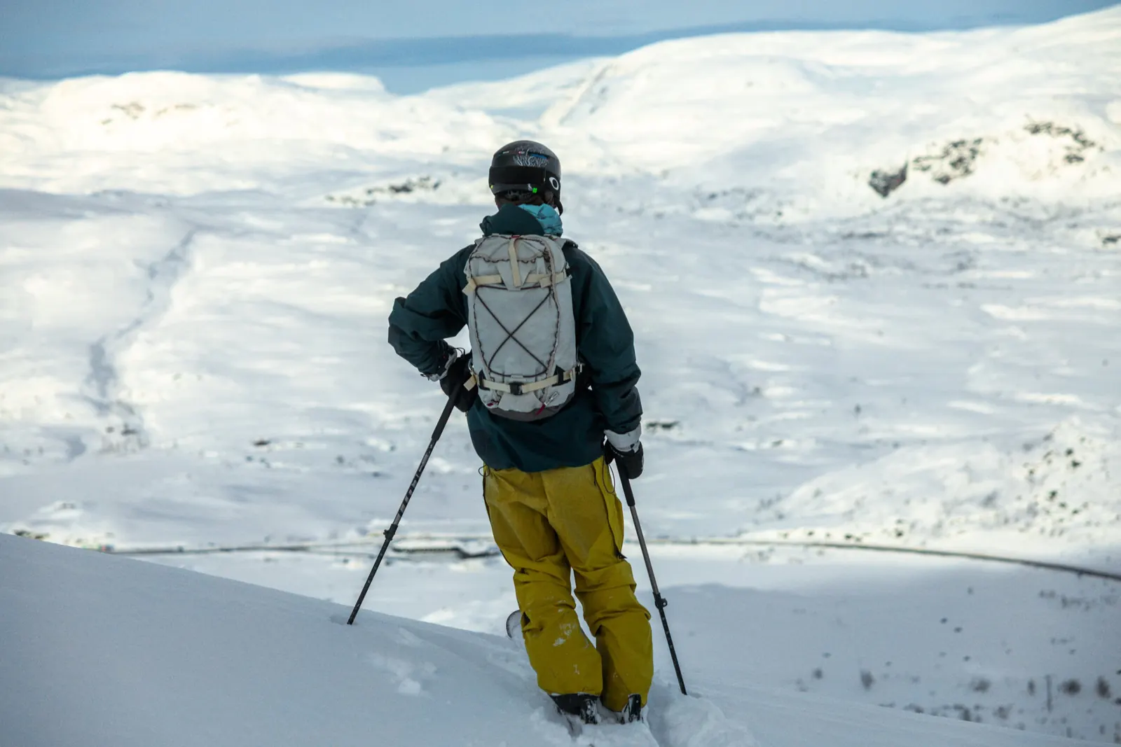 Person mit Rucksack und Stöcken steht auf einem verschneiten Hochplateau