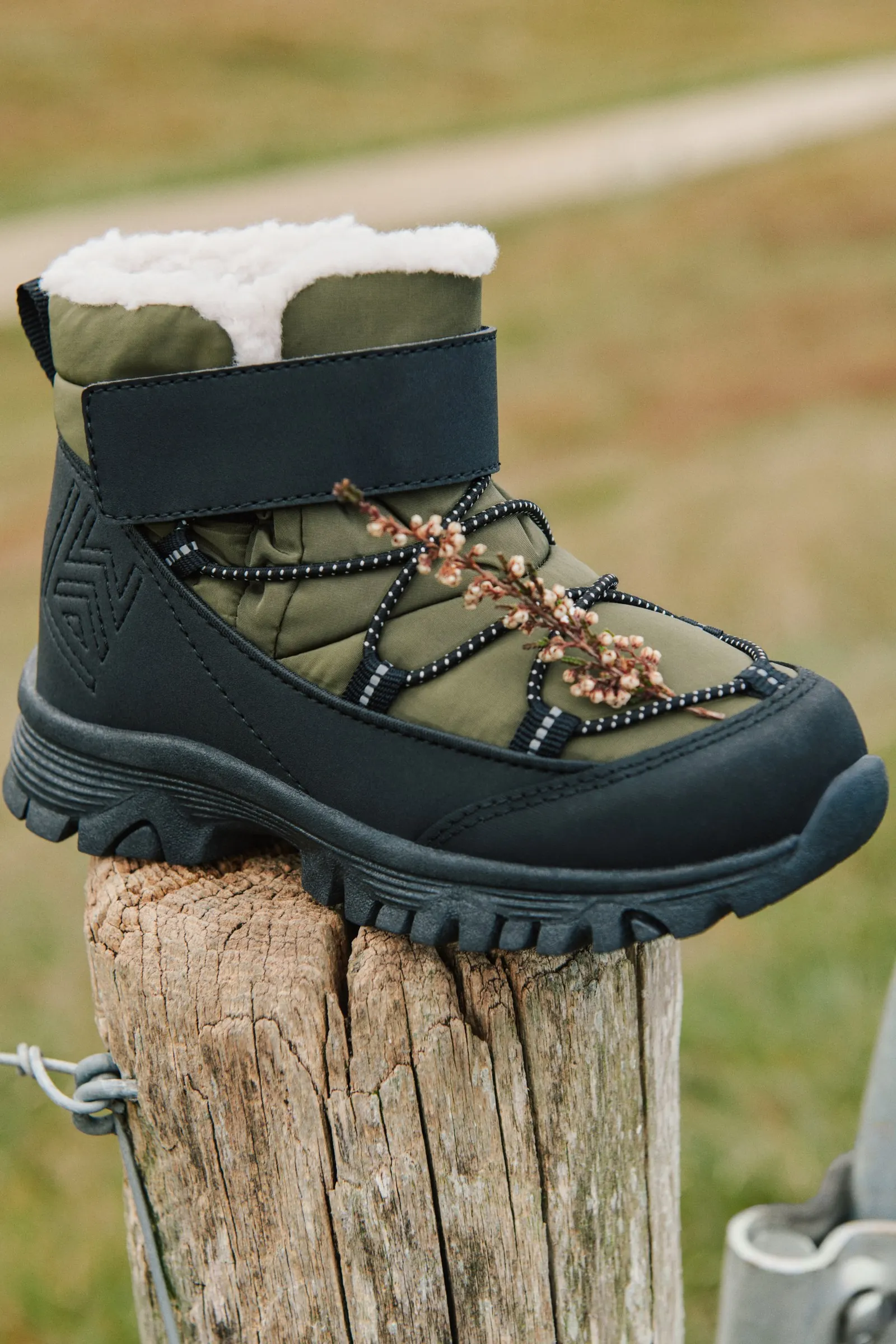 Gefütterter Kinder-Winterstiefel mit elastischer Schnürung und Klettriemen steht auf einem Holzpfahl