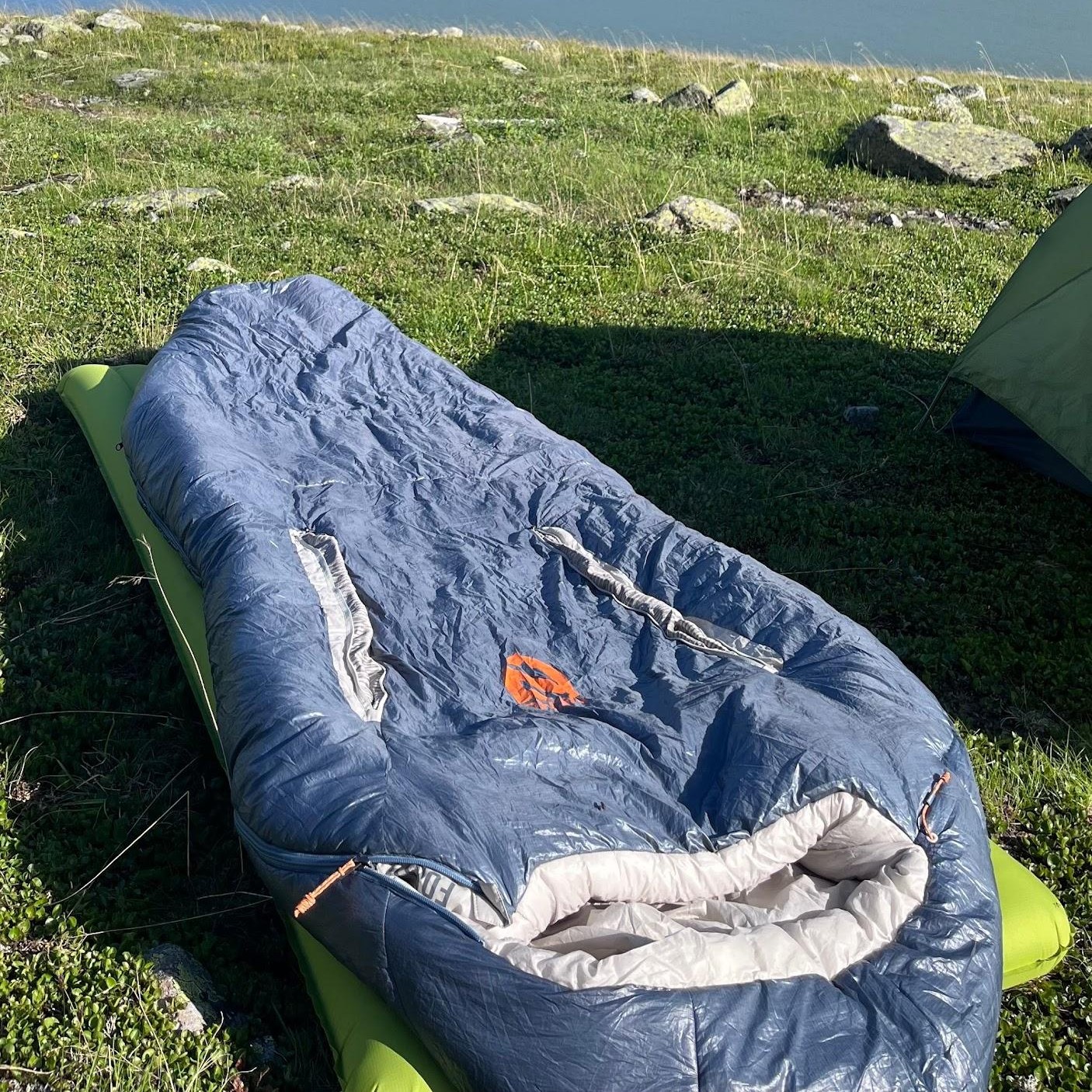 Nemo Forte Schlafsack auf einer Wiese am See, Berge im Hintergrund