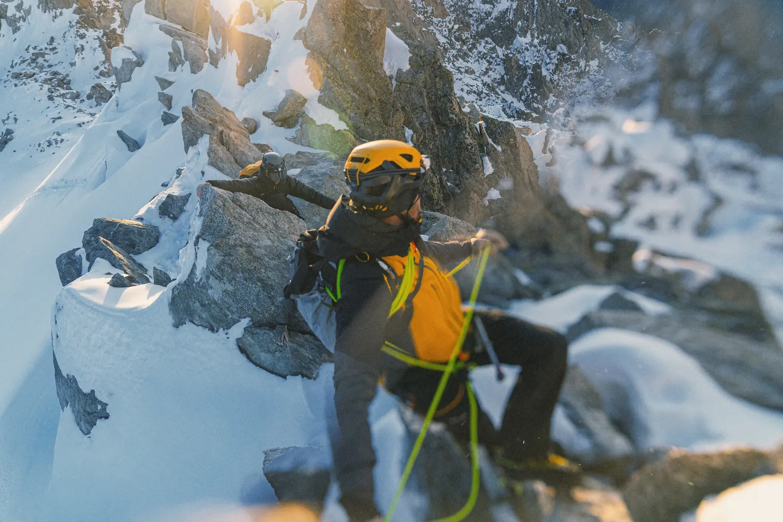 Alpinist im Aufstieg über Fels und Schnee, gesichert mit Seil, im Gegenlicht der Abendsonne