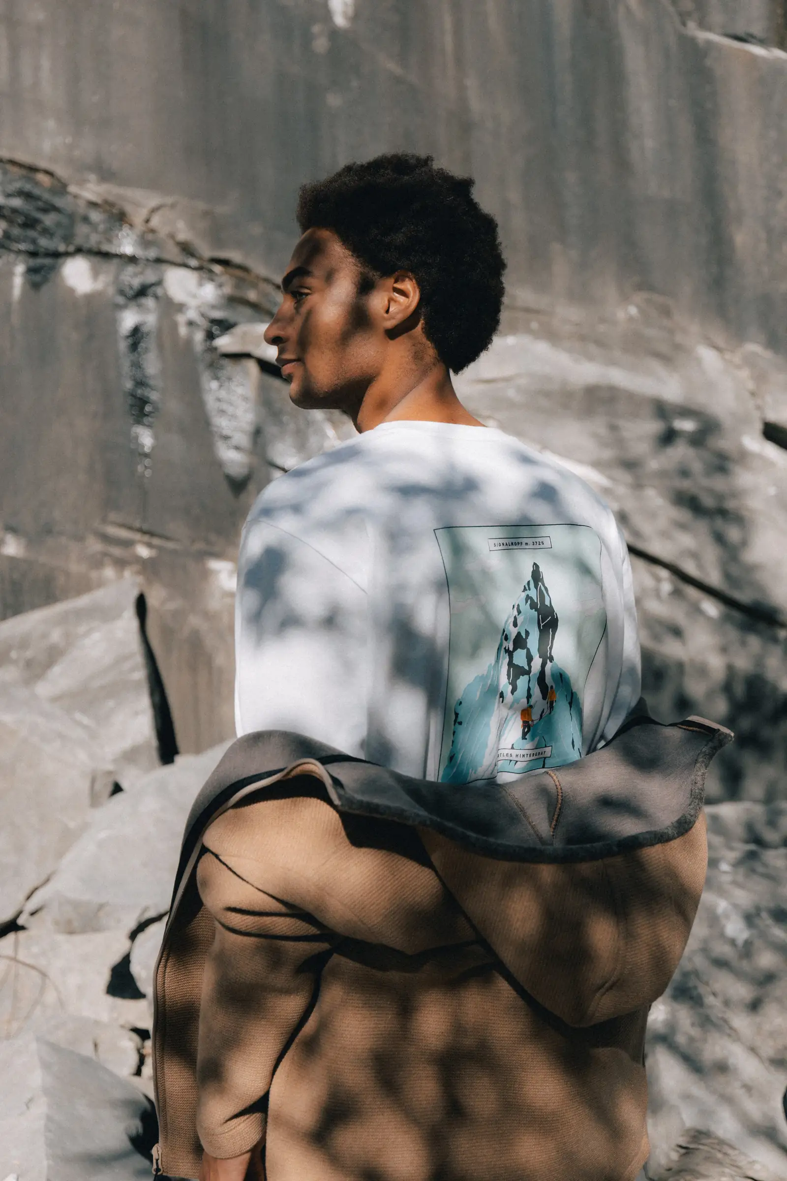 Person trägt eine Fanes-Jacke über dem Arm, Rückenprint mit Bergmotiv "Ortles Hintergrat"
