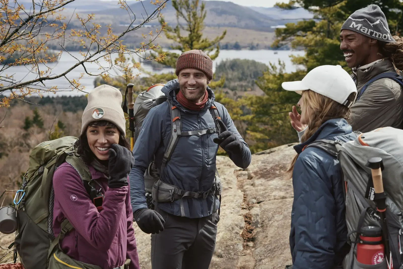 Wandergruppe in Daunen- und Isolationsjacken auf einem Aussichtsfelsen über einem See