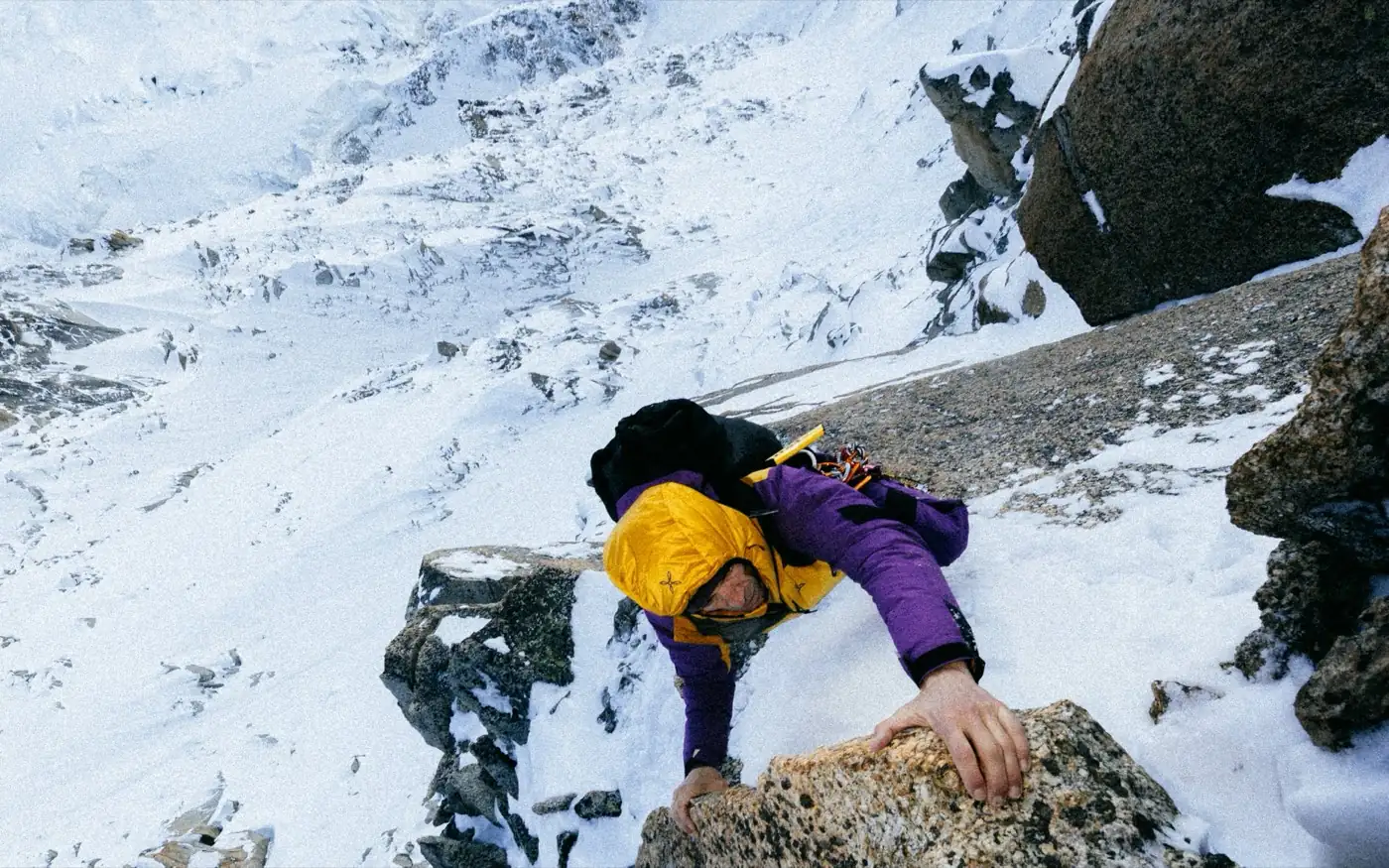 Climber with both hands on the rock, dynamic ascent along a snow-covered ridge