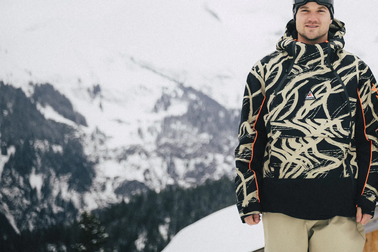 Snowboarder in the O'Neill FWC'Play Asymmetric Snow Jacket and Oversized Snow Pants against a mountain backdrop