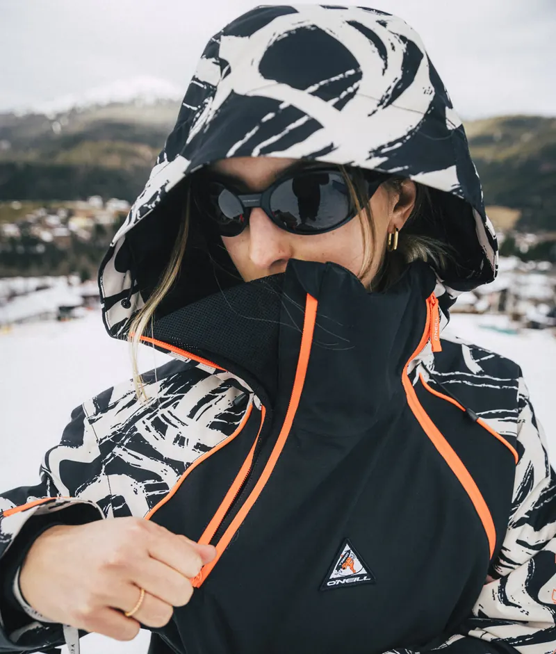 Snowboarderin zieht die Kapuze der O'Neill FWC'Play Asymmetric Snow Jacket über