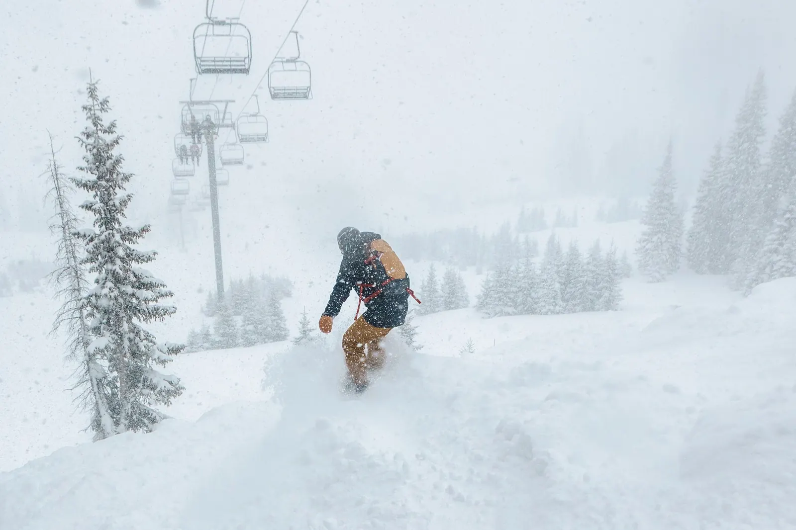 Snowboarder mit Osprey-Rucksack im Tiefschnee unter einem Sessellift