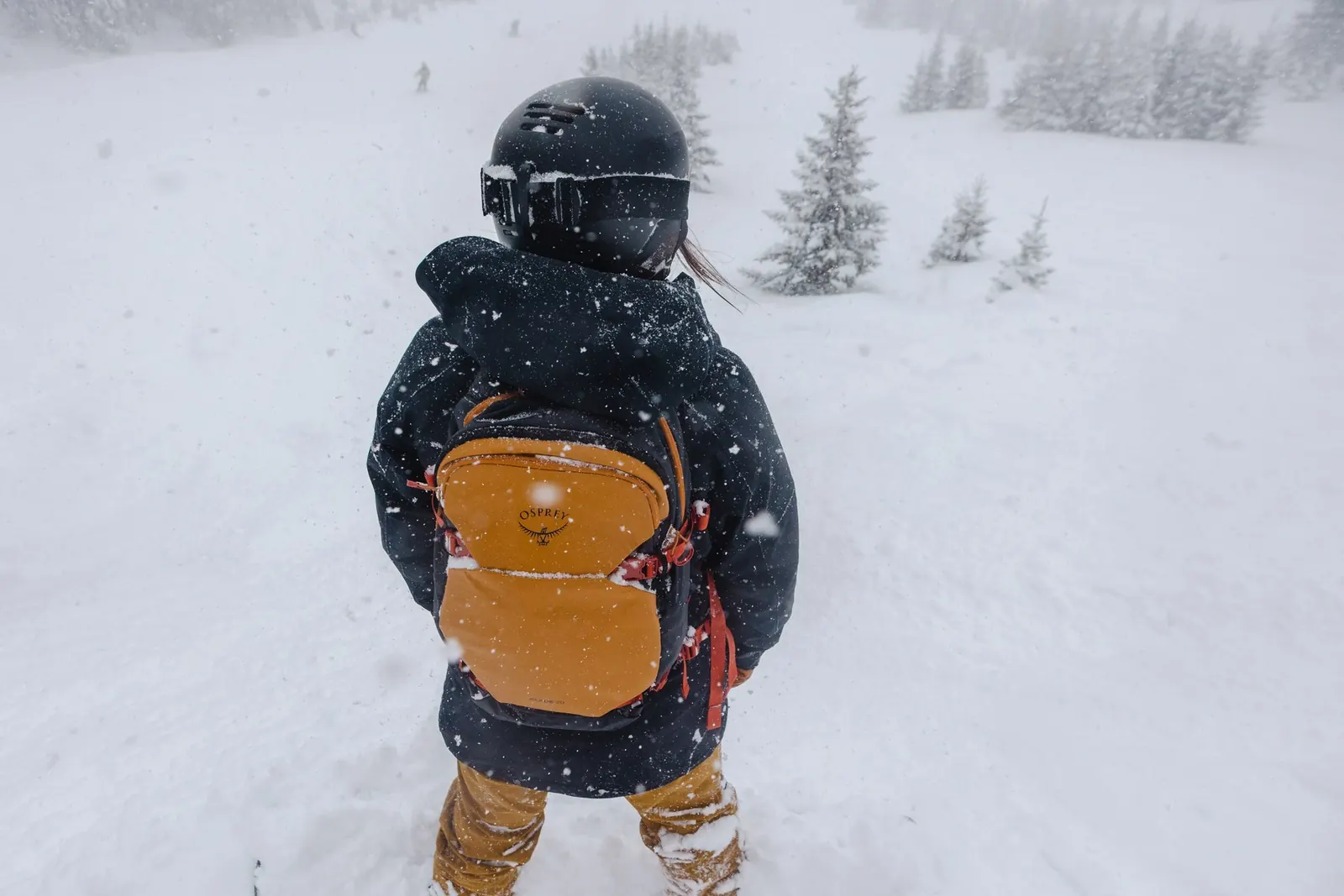 Osprey Glade 12 auf dem Rücken einer Person mit Snowboard im Schneetreiben