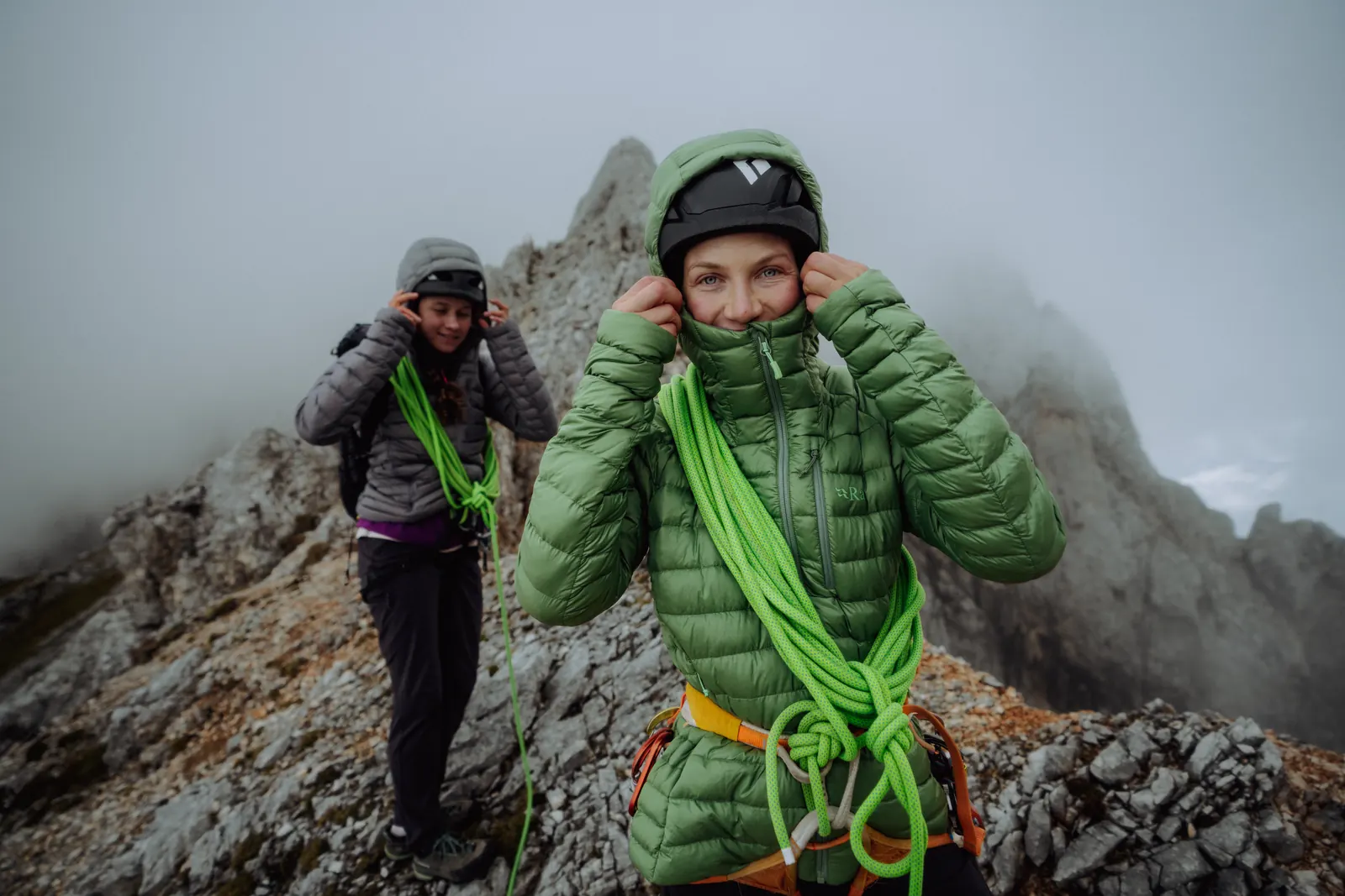 Two climbers on a ridge, the one in front wearing the green Rab Microlight Alpine Hoody with helmet and rope