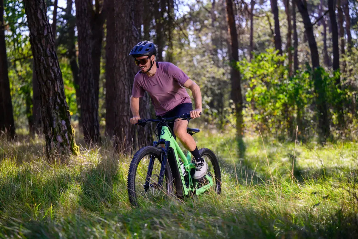 Felix Neureuther fährt mit einem hellgrünen Scott-E-Mountainbike durch einen sonnigen Kiefernwald