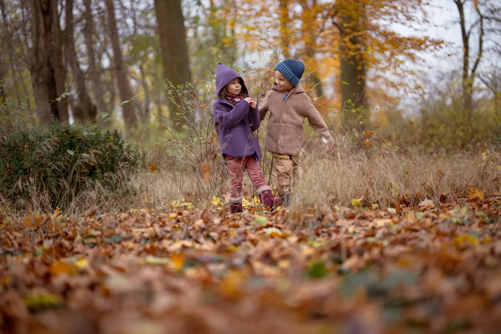 Zwei Kinder in Jacken und Mützen laufen durch das Herbstlaub