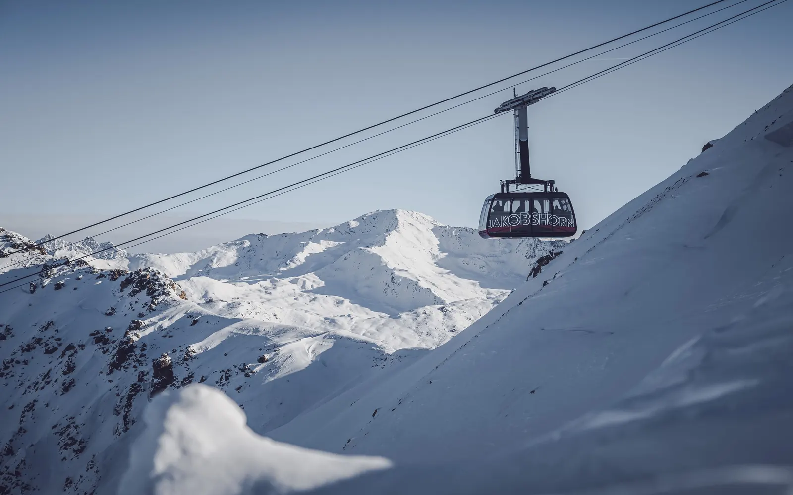 Kabine der Luftseilbahn mit der Aufschrift Jakobshorn vor verschneiten Bergen