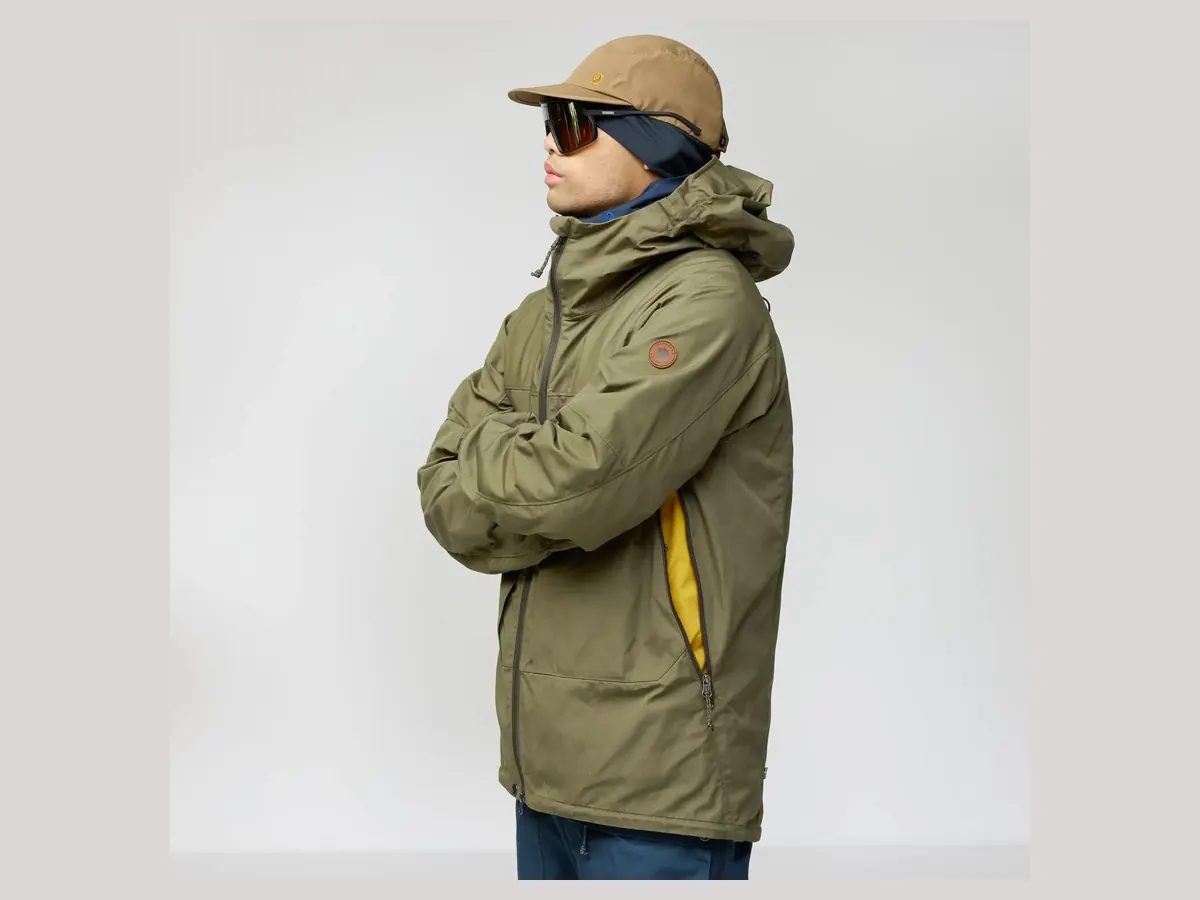 Mann in olivgrüner Fjällräven Bergtagen G-1000 Jacket mit Kapuze, Kappe und Sonnenbrille