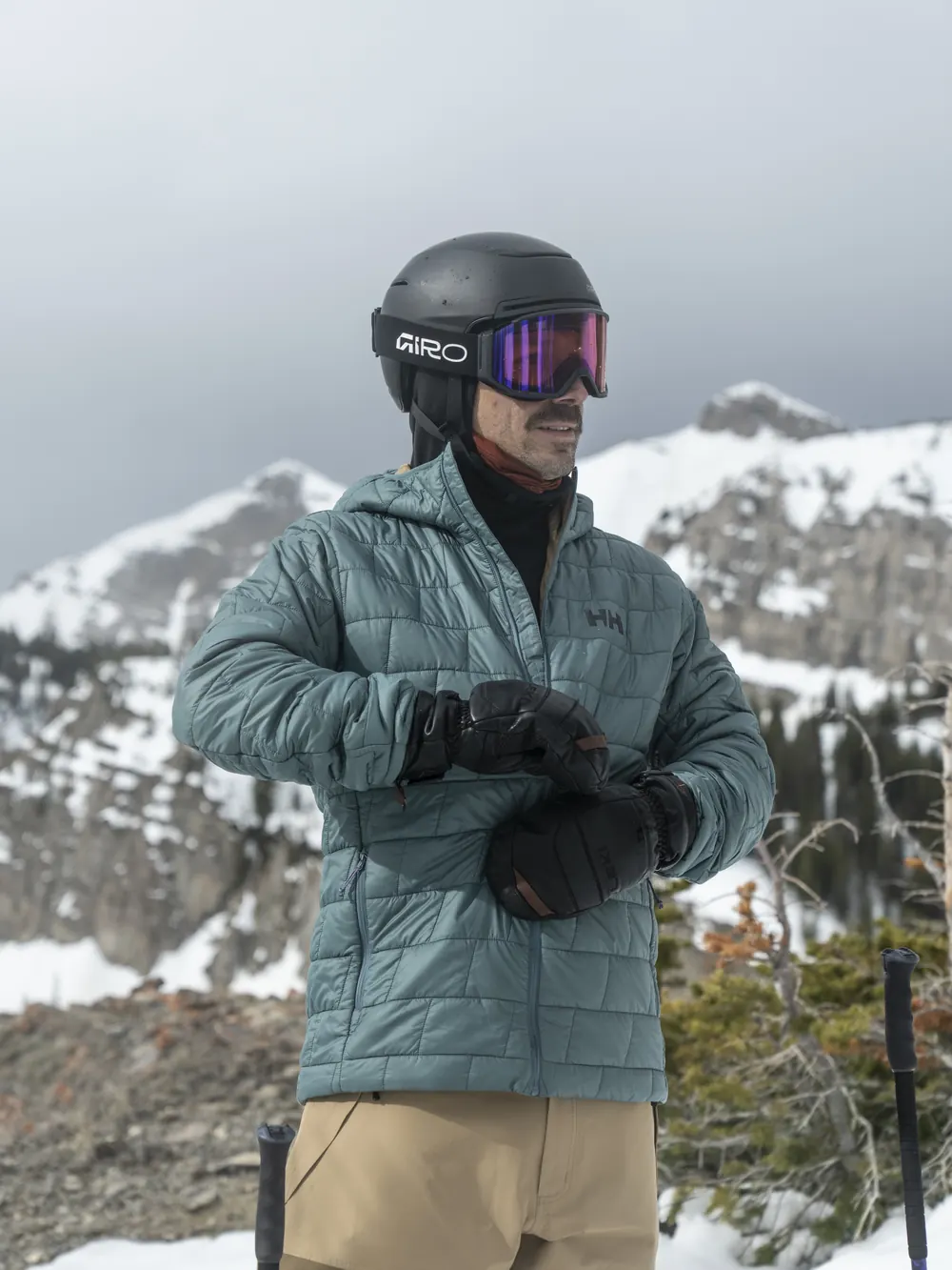 Skier in a quilted Helly Hansen insulated jacket fastening his gloves in the mountains