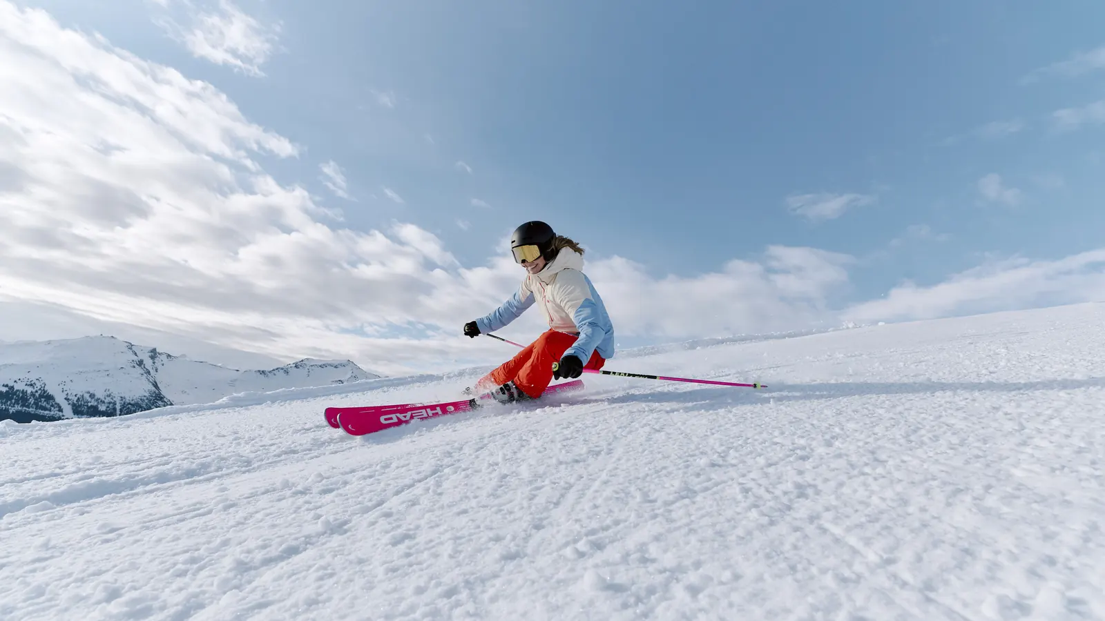 Skier in a light blue and white Helly Hansen ski jacket carving on the piste