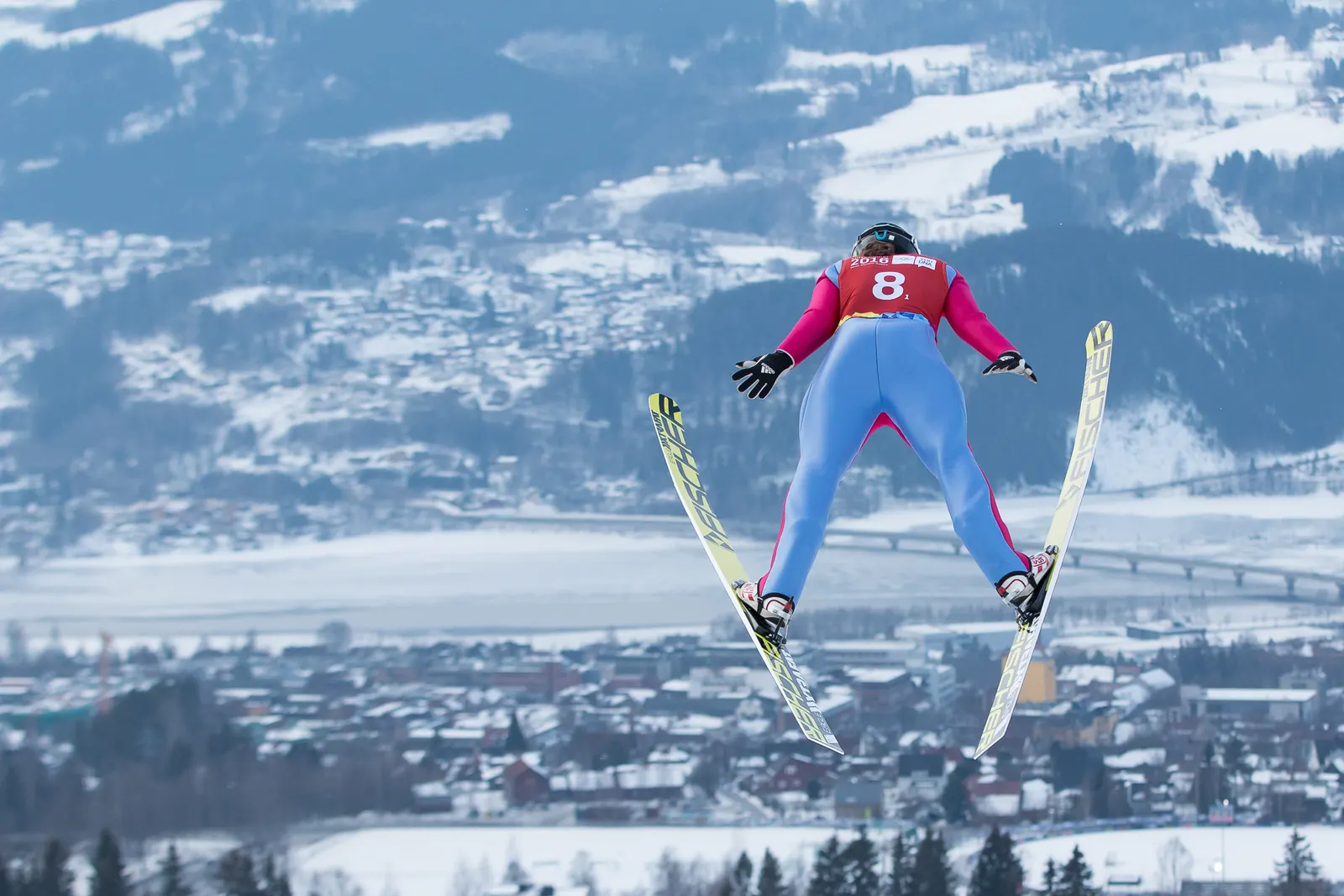 Skispringerin im Flug über der verschneiten Stadt Lillehammer