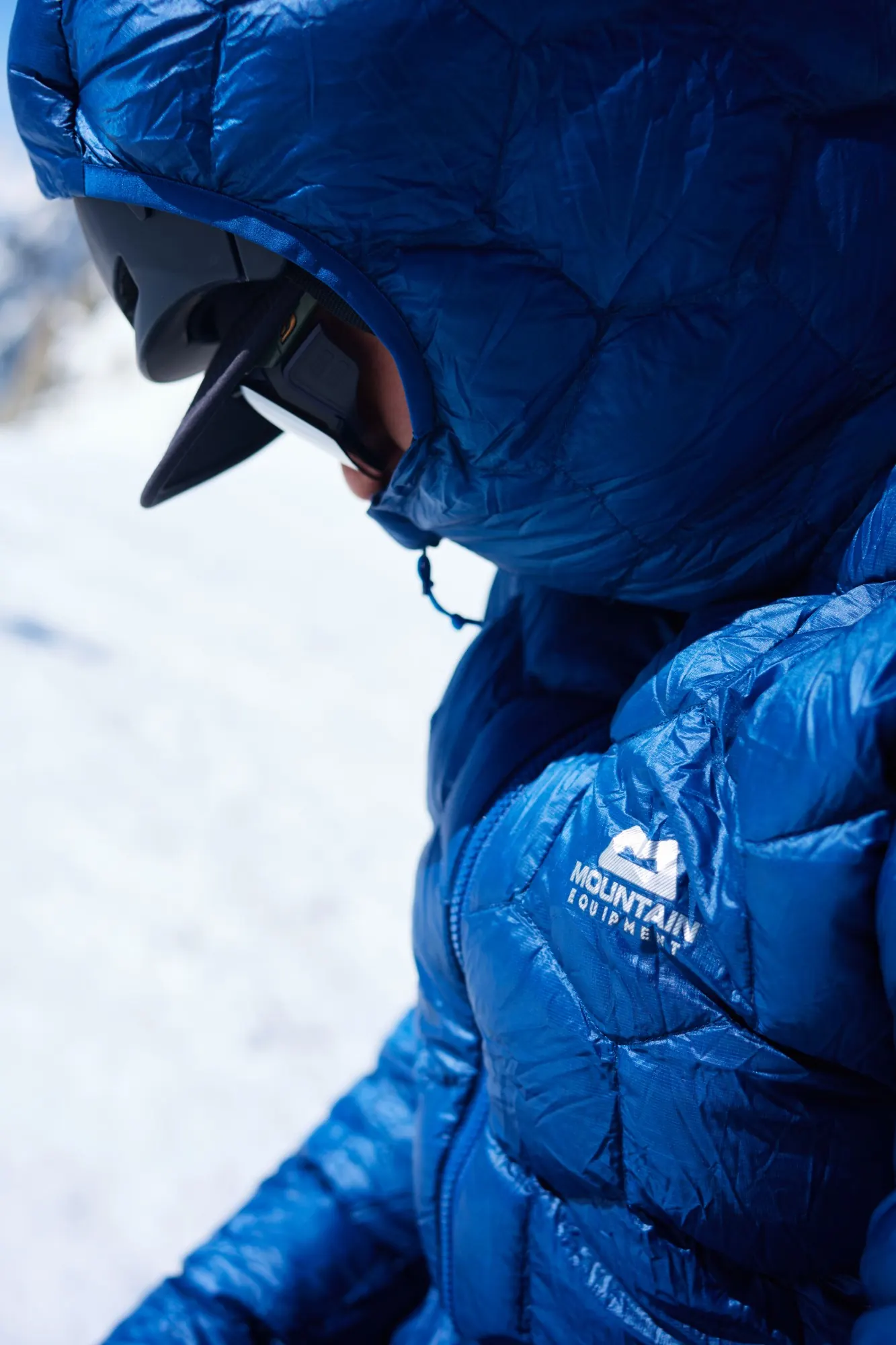 Side close-up: hood of the blue Xenith down jacket over a climbing helmet