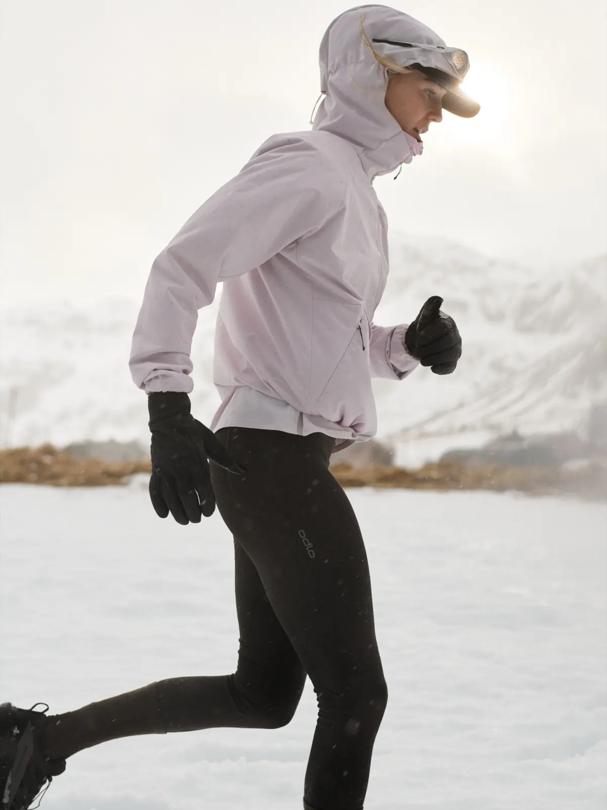 Läuferin mit Kapuze, Handschuhen und Tight läuft durch eine verschneite Landschaft