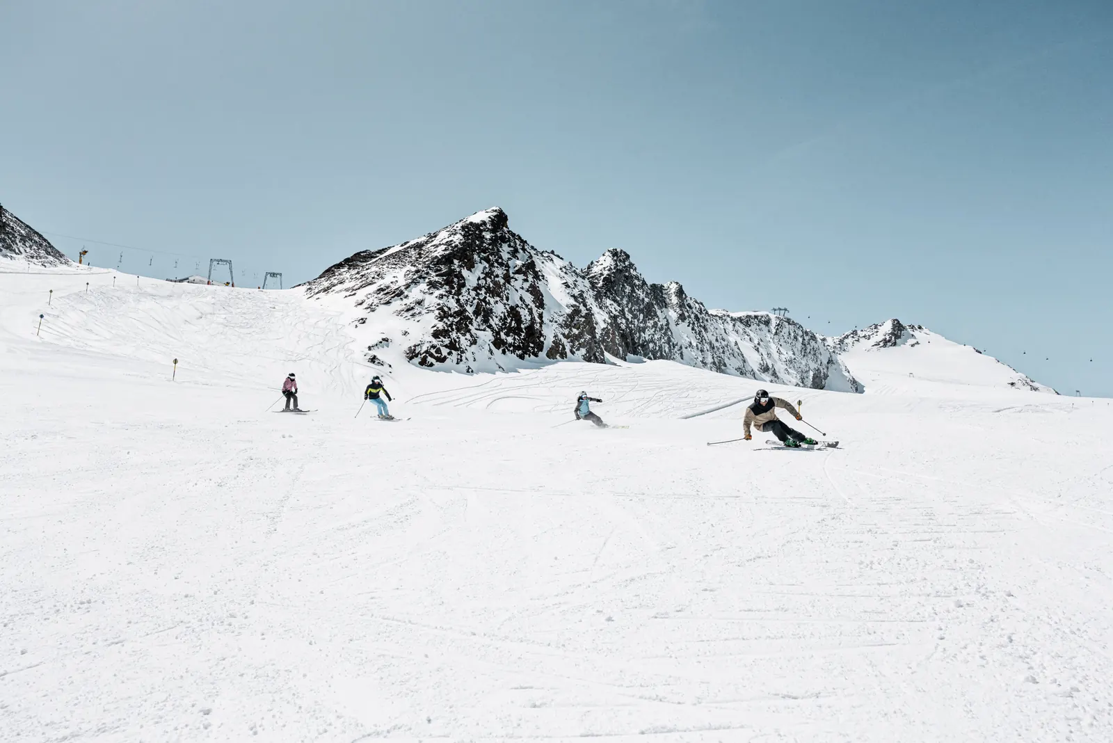 Mehrere Skifahrer auf einer breiten Gletscherpiste am Rettenbachferner, dahinter ein Felsgipfel