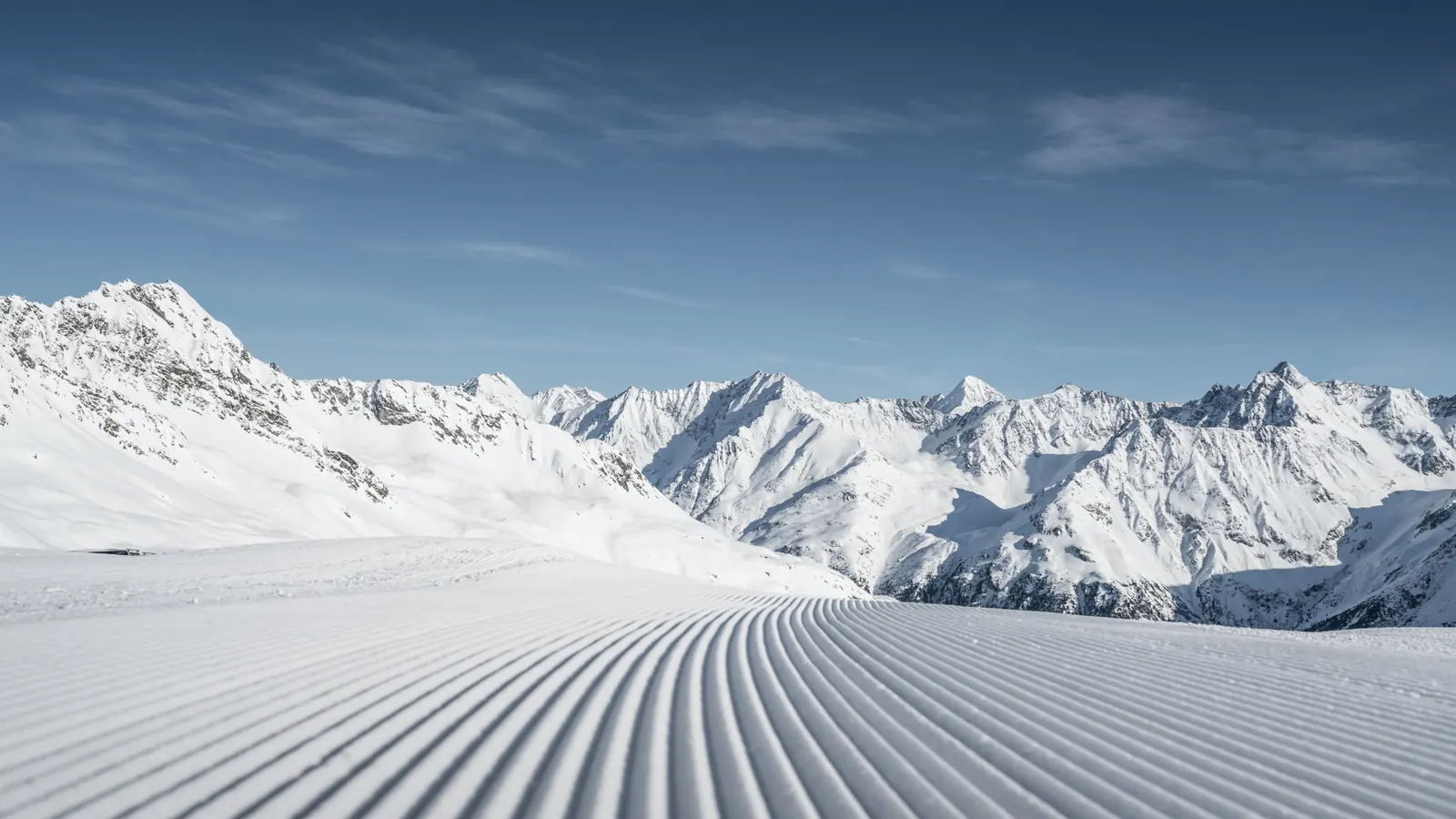 Frisch präparierte Piste mit Kordstruktur, dahinter verschneite Gipfel