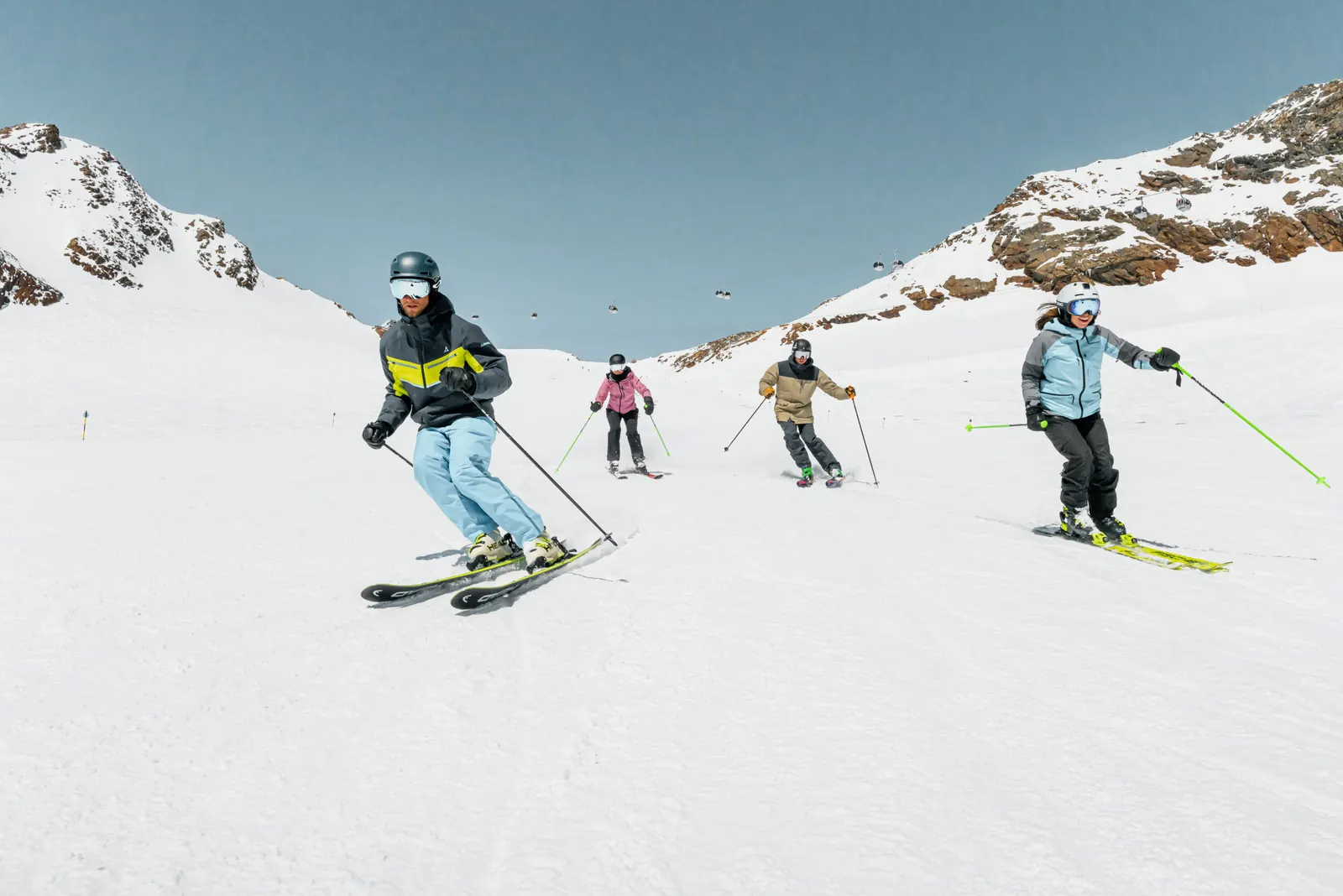 Vier Skifahrer fahren gemeinsam einen flachen Gletscherhang hinunter