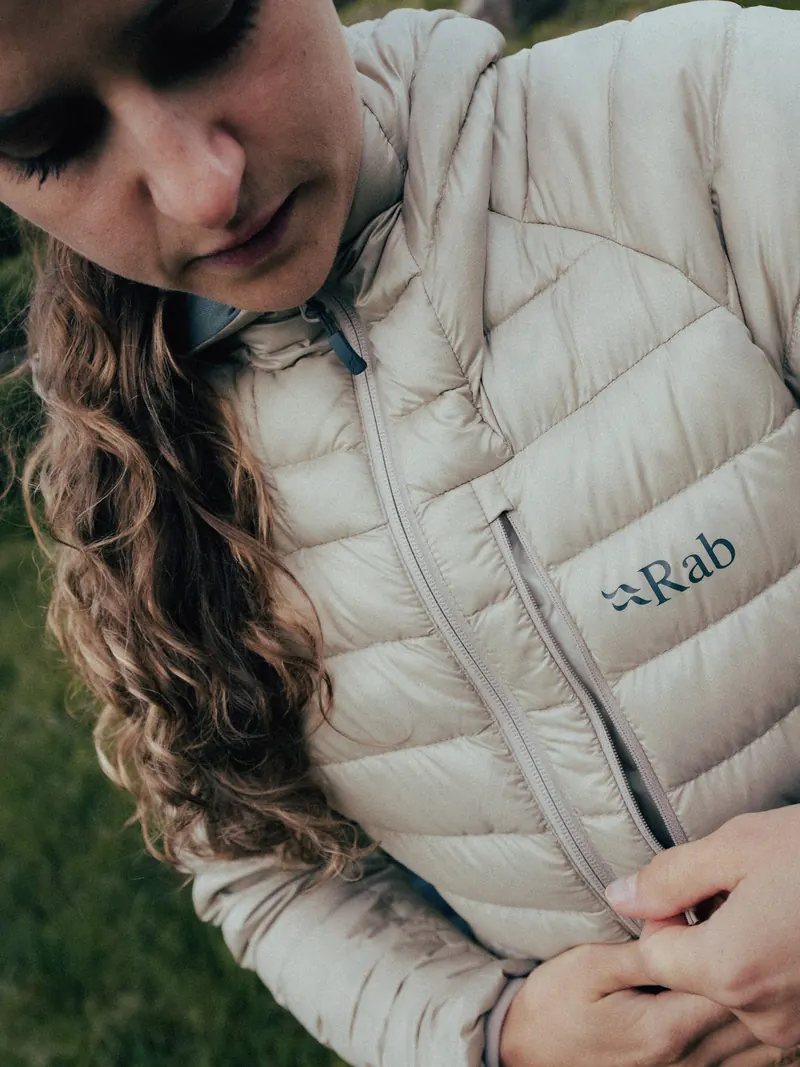 Woman zipping up a beige Rab Microlight Alpine
