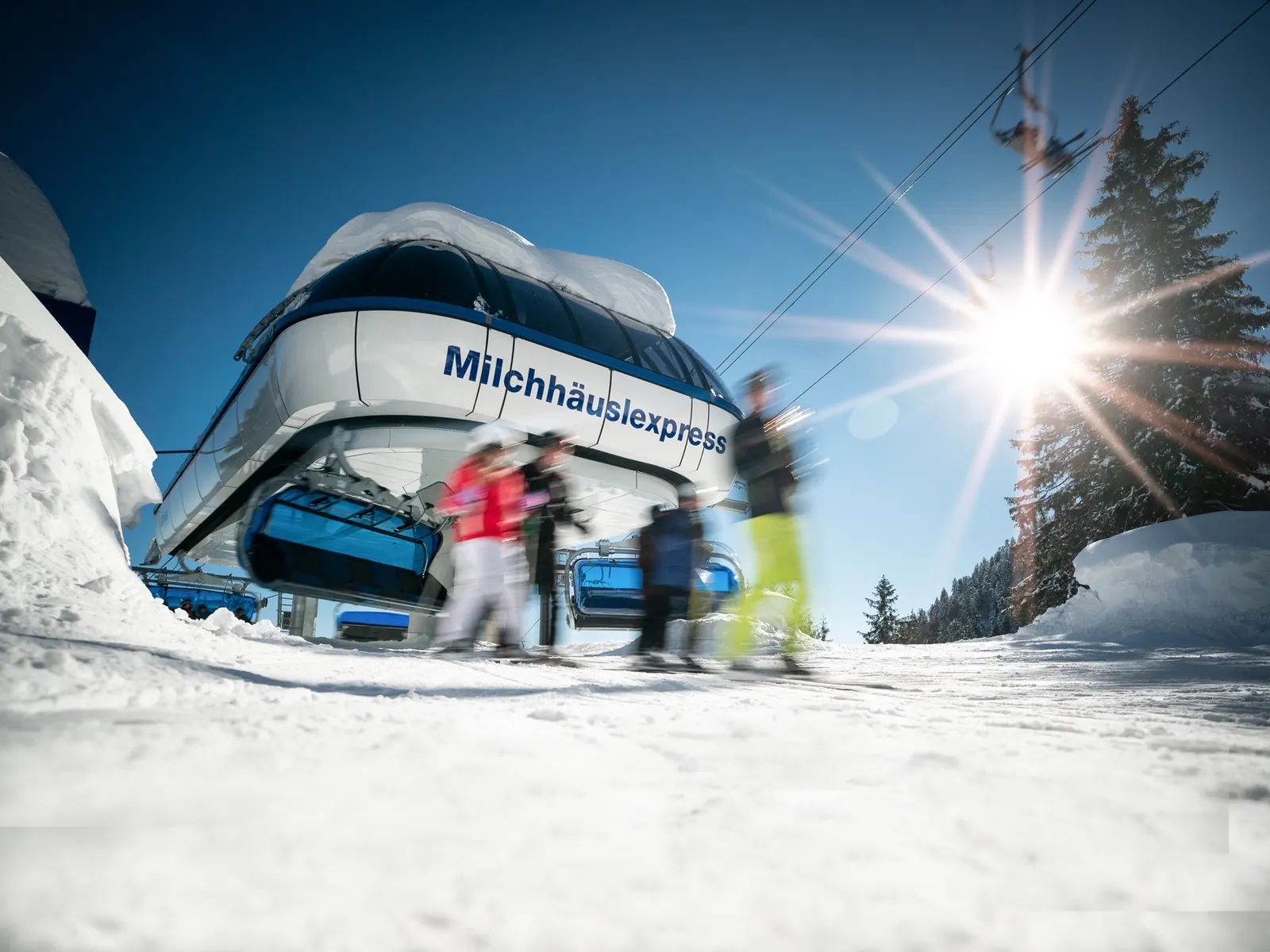 Skifahrer steigen an der Station der Sechser-Sesselbahn Milchhäuslexpress am Brauneck aus, die Sonne steht tief