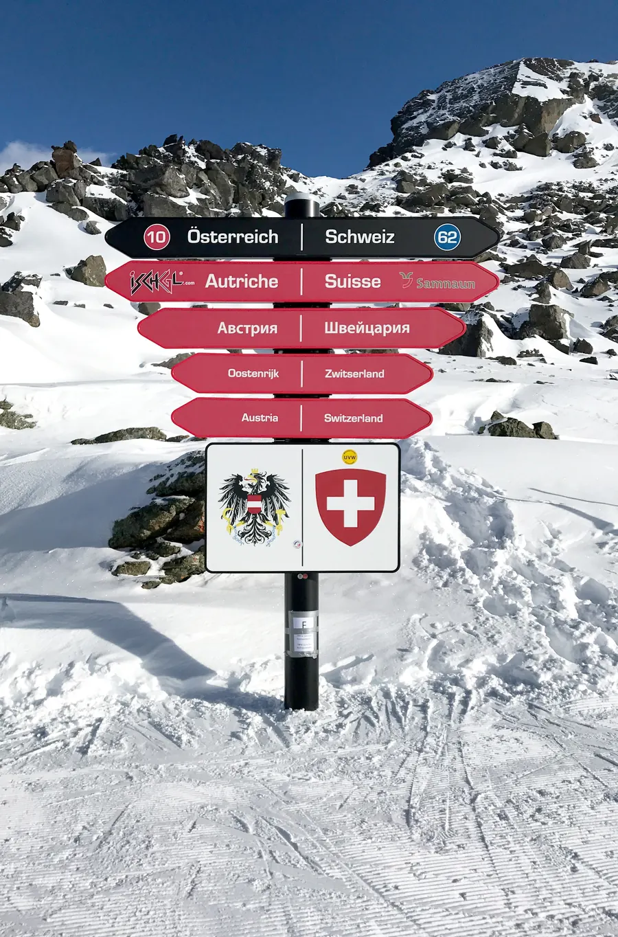 Wegweiser an der Piste mit den Aufschriften Österreich und Schweiz, darunter die Wappen beider Länder