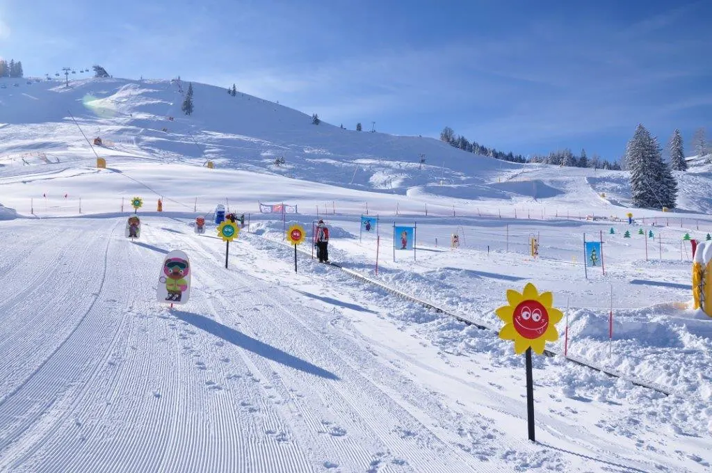 Übungsgelände im Kinderland mit bunten Figuren und Fähnchen auf einer flachen, präparierten Schneefläche